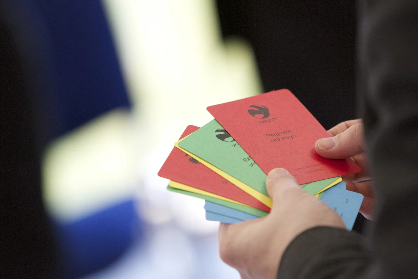 Person holding a colorful set of cards with words such as 'Insights' and phrases like 'Pragmatic and tough'.