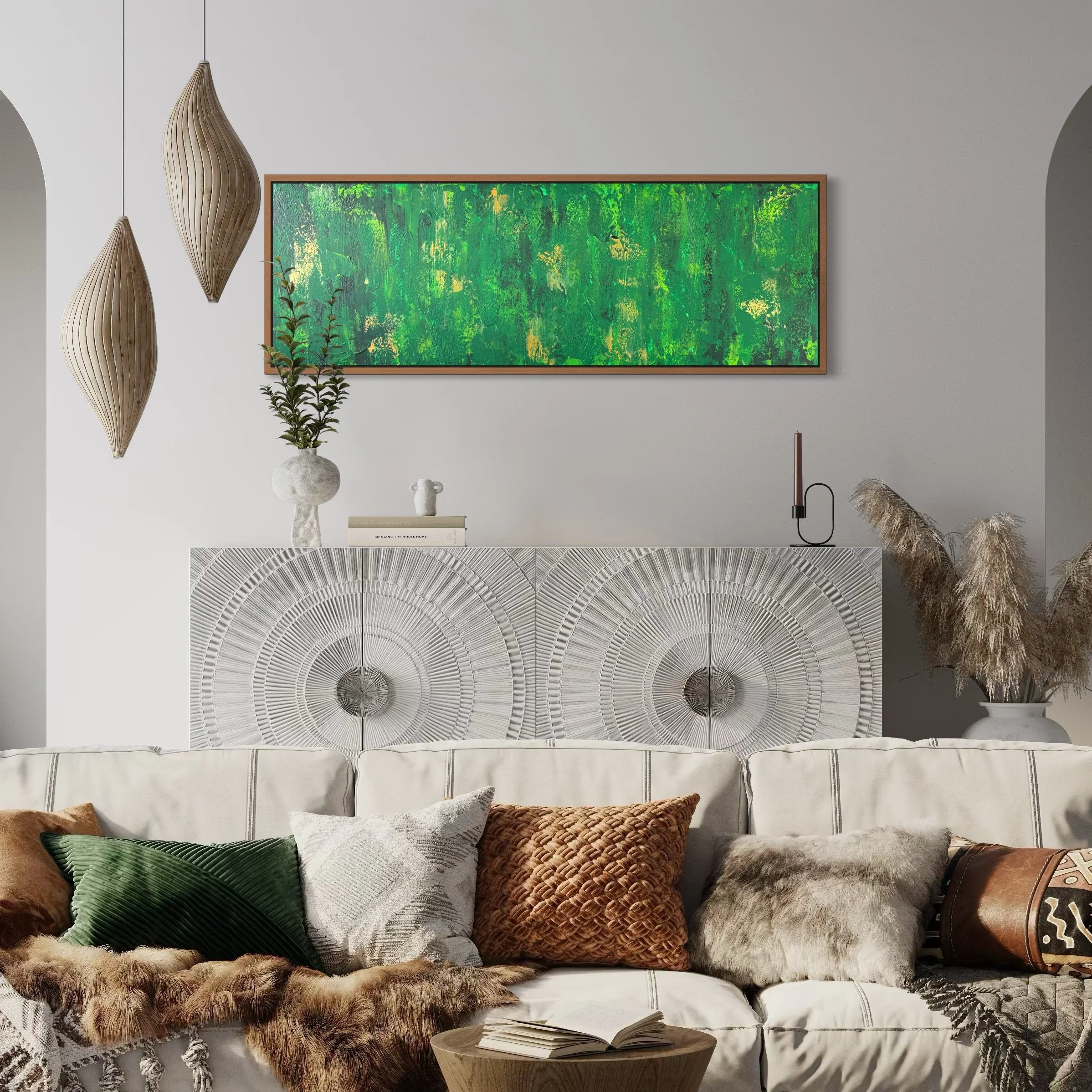 Intérieur moderne avec un canapé blanc, des coussins en différentes textures et couleurs, une table en bois avec un livre ouvert, décorations vertes et naturelles, peinture abstraite verte, et éclairage suspendu en bois