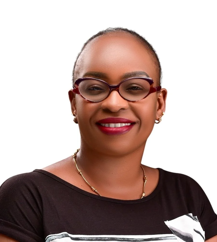Portrait of a woman with glasses, earrings, and a necklace, smiling, wearing a black shirt with a white graphic design, against a plain white background.