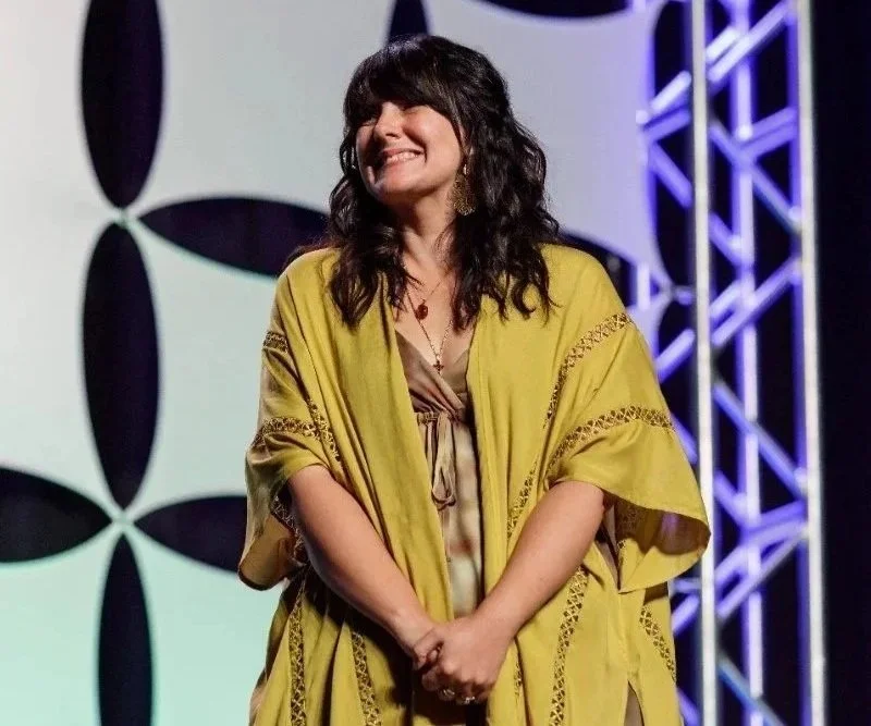 A woman smiling on stage with a geometric black and white background and blue stage lighting.
