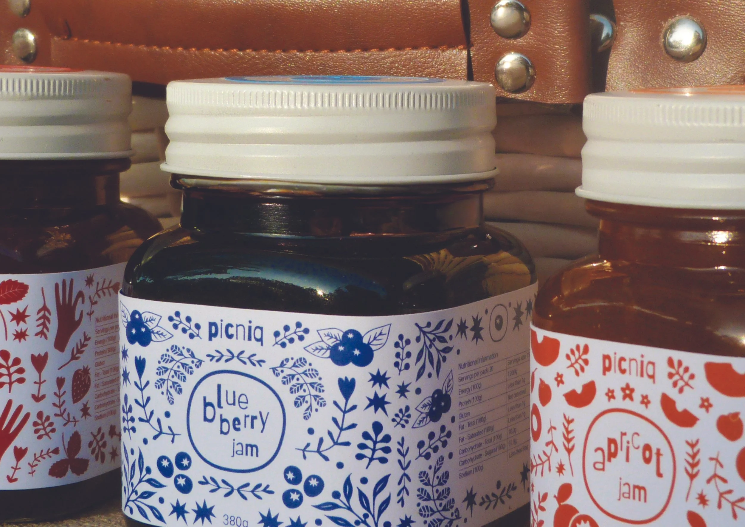 Jars of jam with decorative labels, including blueberry and apricot jam, on a shelf.