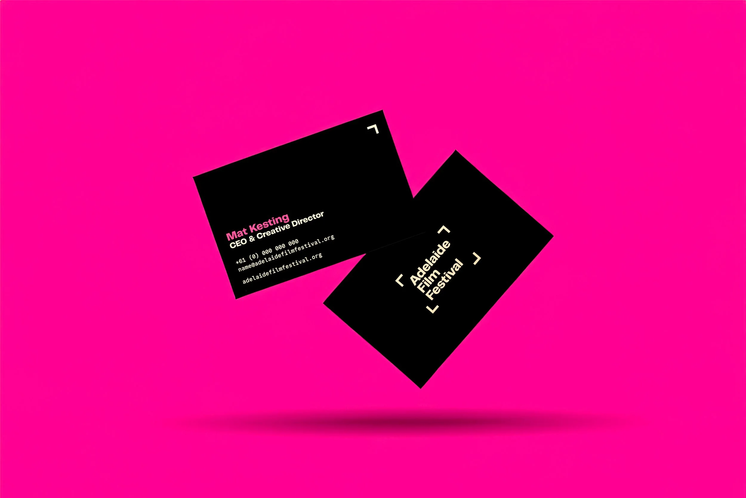 Business cards for Adelaide Film Festival with black backgrounds and white and pink text, floating against a pink background.