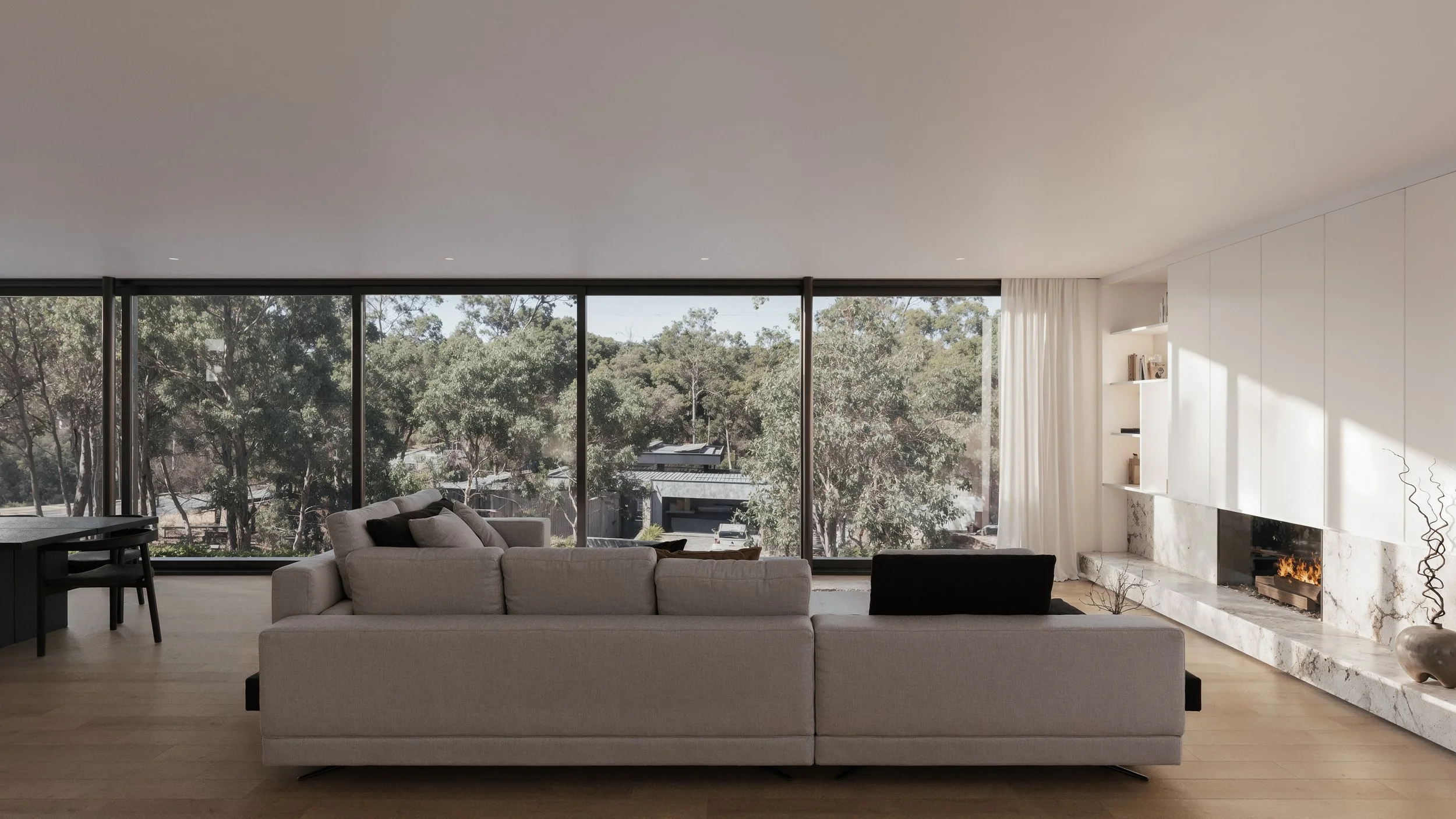 architectural interior render of luxury, modern open-plan living room with large glass floor-to-ceiling windows, grey sofa, and marble fireplace. 