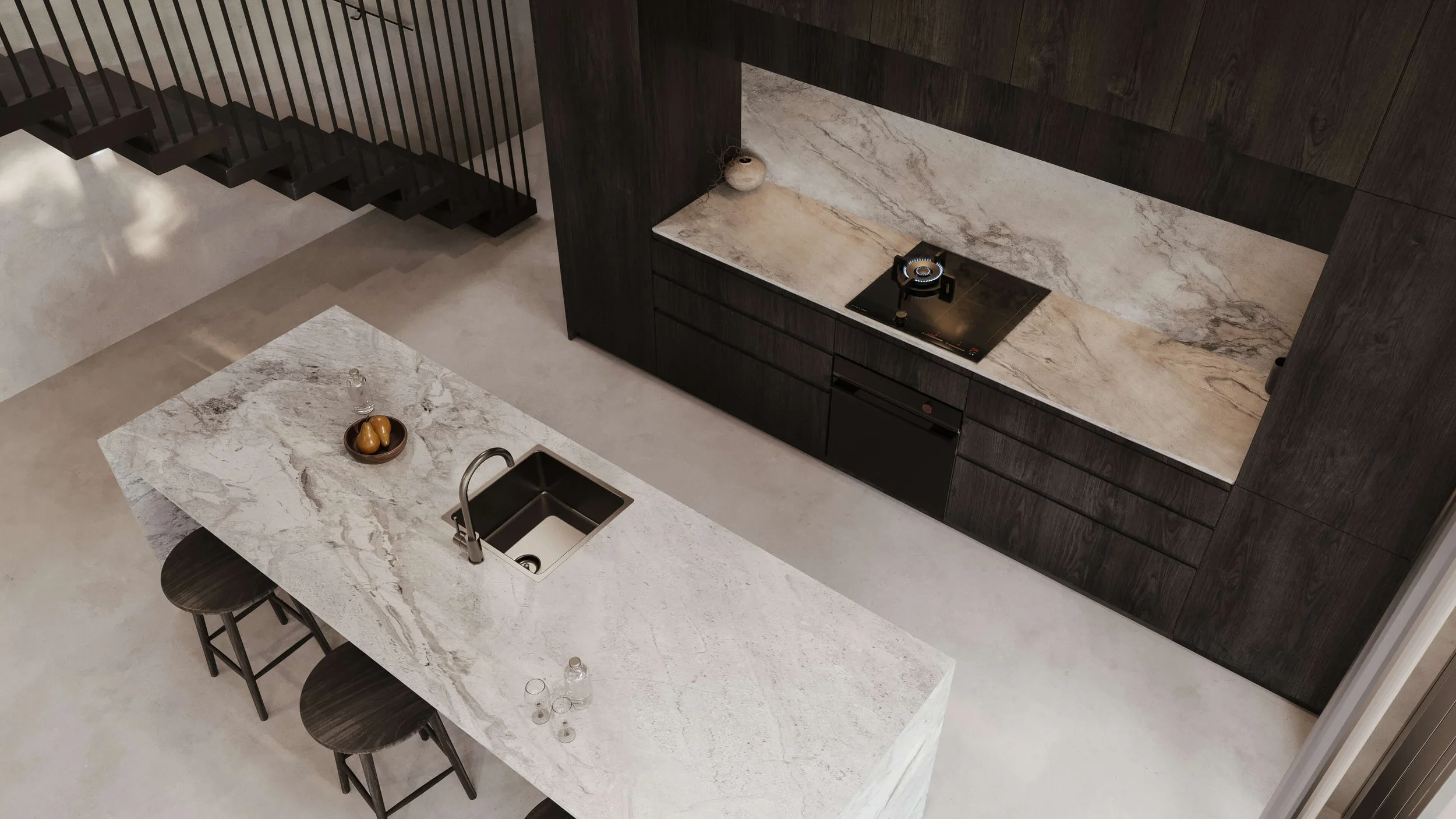 A modern kitchen with a light-colored marble island, black stools, and dark wood cabinetry. The marble countertop of the island has a sink and a bowl with fruit. The wall behind has a built-in stovetop with a small pot and decor item.