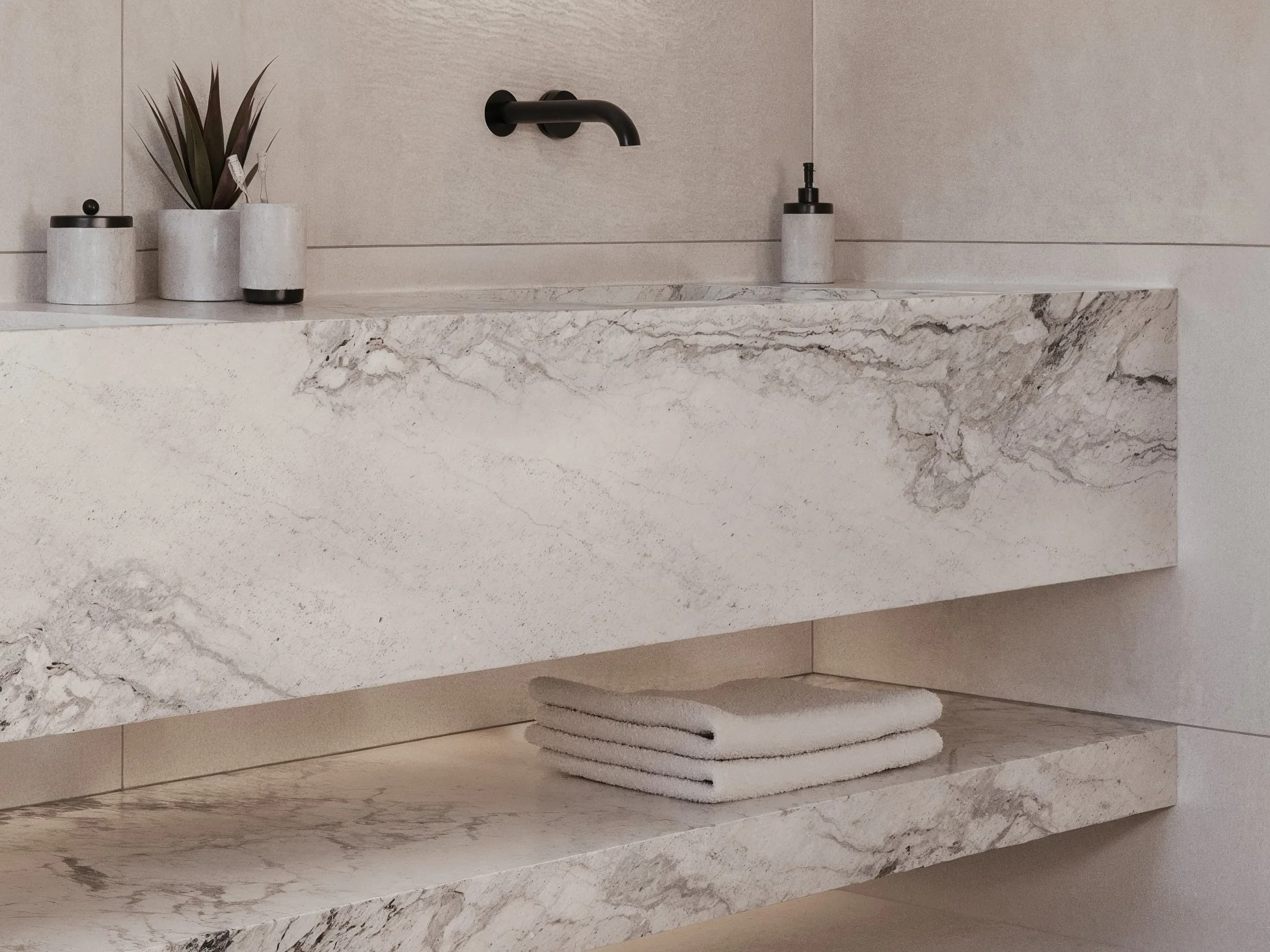 Minimalist bathroom with a marble vanity, black faucet, a soap dispenser, a toothbrush holder, and stacked white towels underneath.