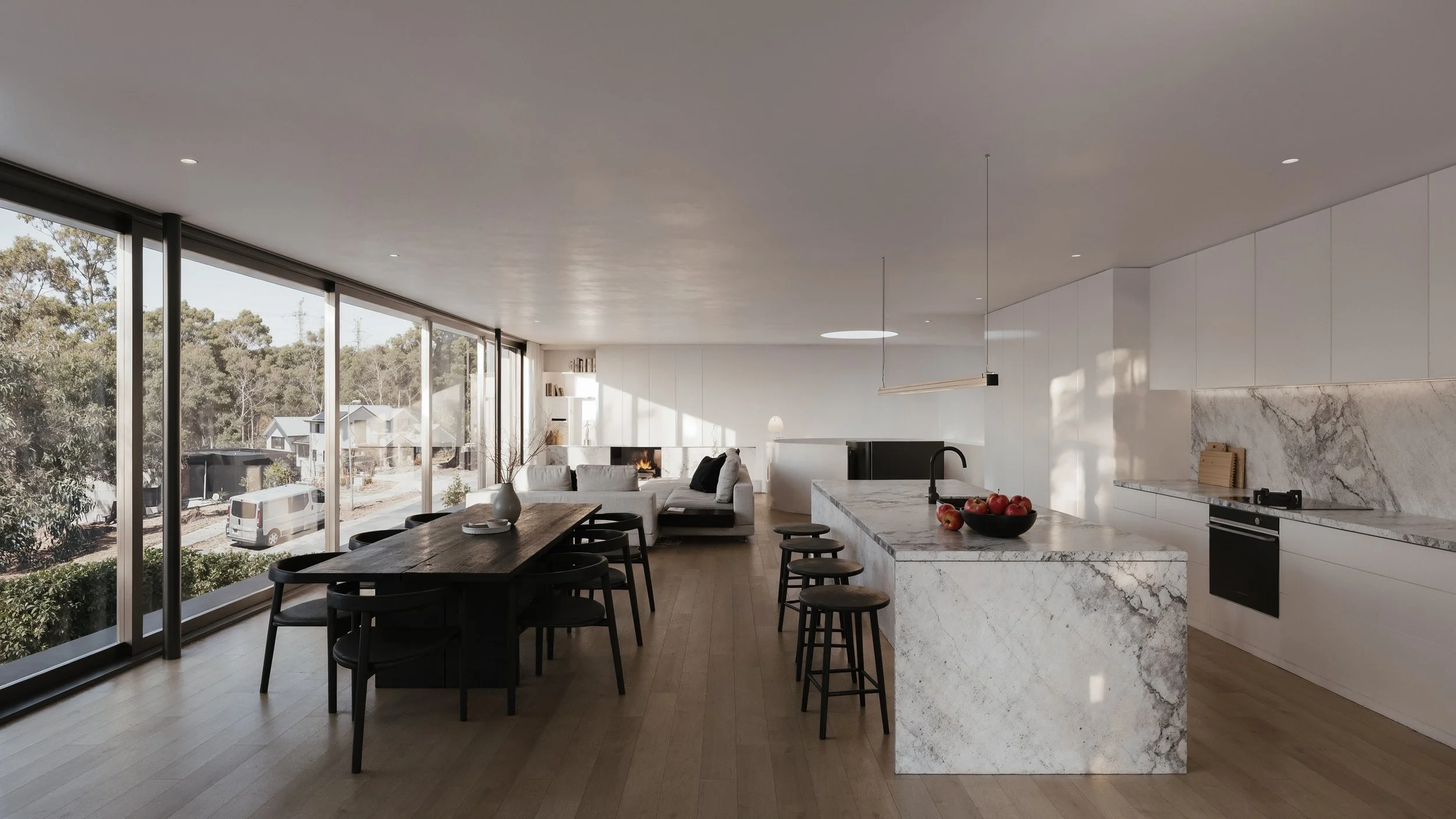 Modern open-concept living room and kitchen with large windows, white cabinetry, marble island, black appliances, and minimalist decor.