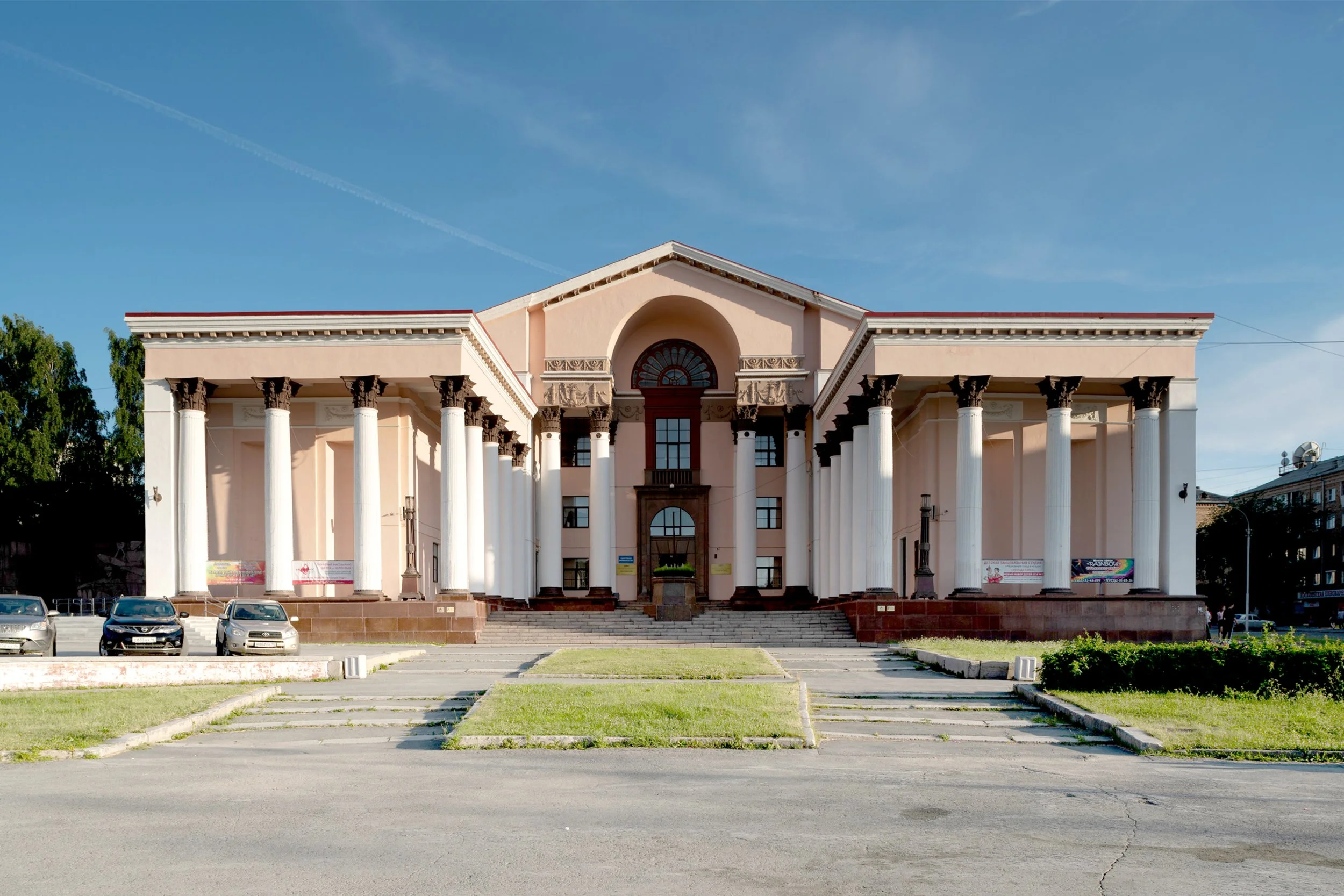 A neoclassical building with large white pillars, pink walls, and a central arched entrance.