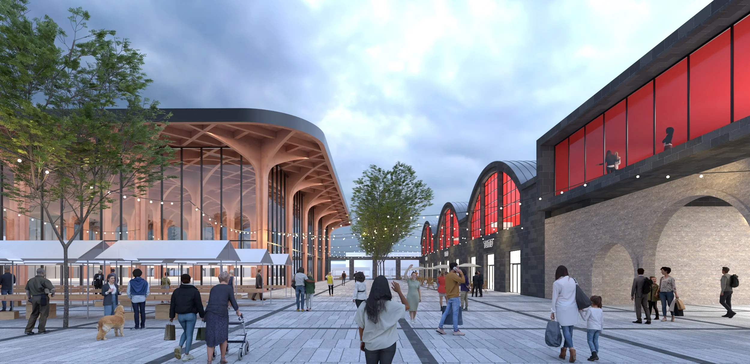 People walking and shopping in an outdoor marketplace with modern and industrial architecture, large trees, and string lights overhead during daytime.