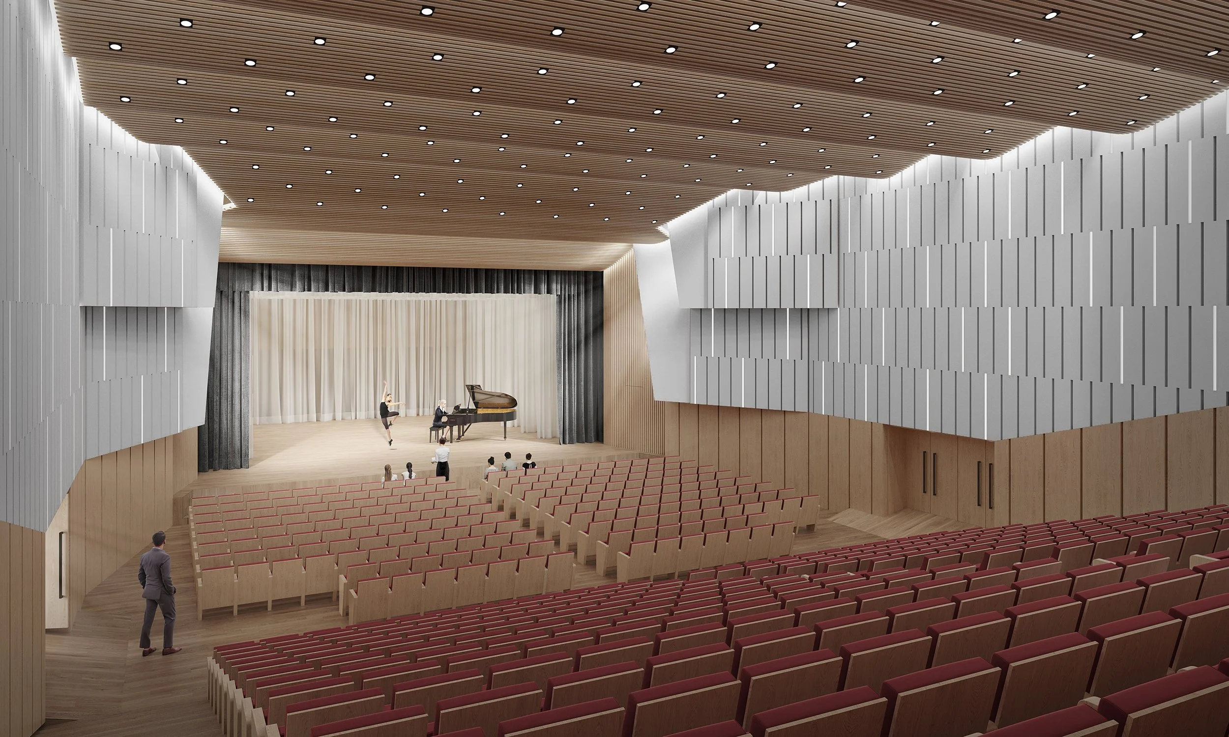 Modern auditorium with wooden walls and ceiling, beige stage with a white curtain, a pianist at a grand piano, a ballet dancer practicing, and a few people seated. Red seats in the foreground.