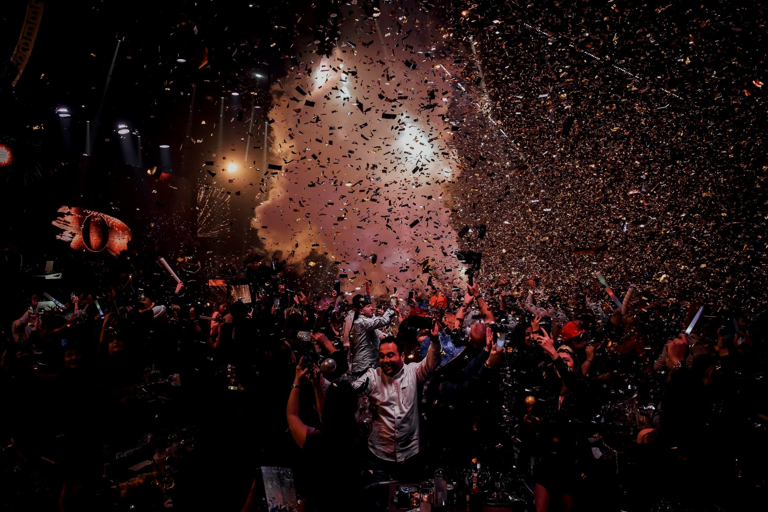 People dancing and celebrating at a party with confetti, smoke effects, and bright lights.