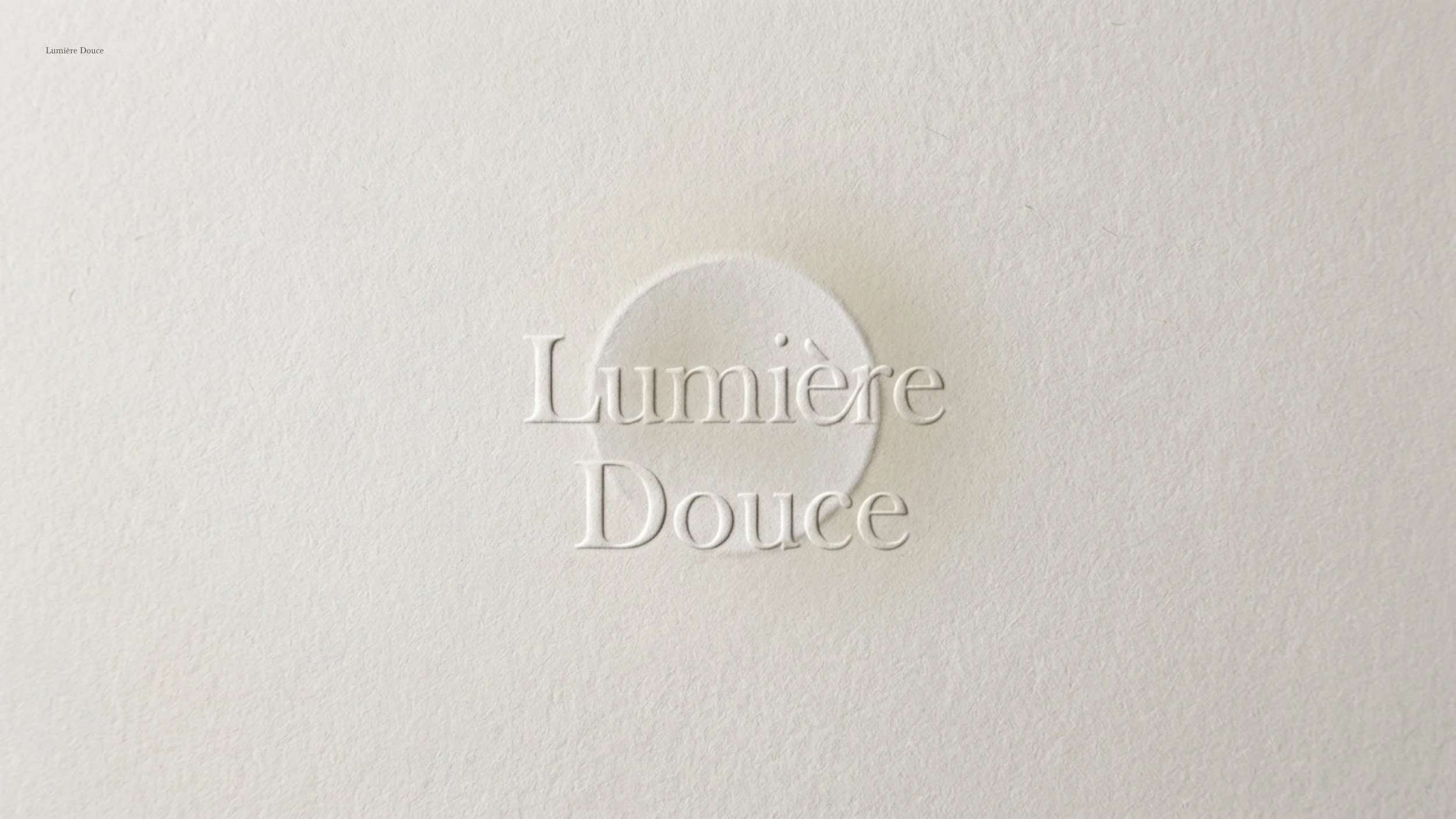 Close-up of embossed white text on a white textured background reading 'Lumière Douce' with a small circle behind the text.