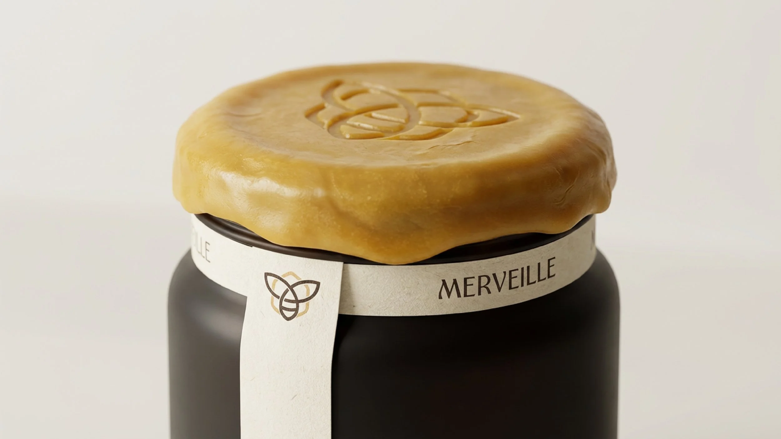 A jar with a black body and a white label that has a bee logo and the word 'MERVEILLE' on it, topped with a piece of caramel or butterscotch