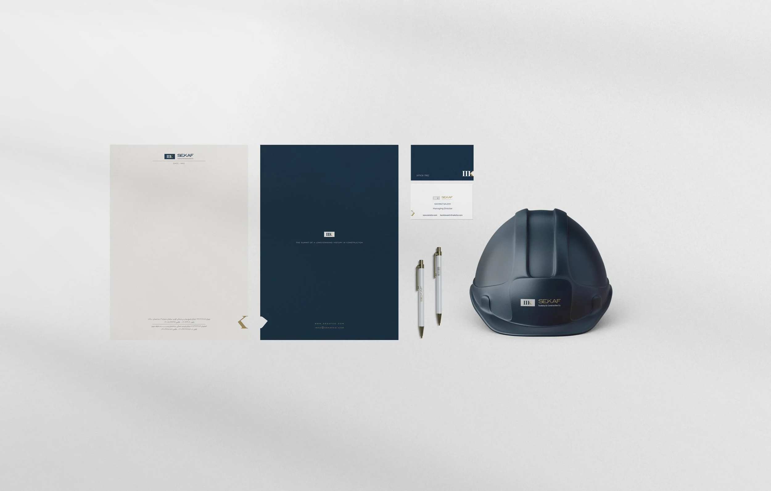 Office supplies including a white folder, a navy folder, a business card, two pens, and a black helmet with a logo, arranged on a white surface.