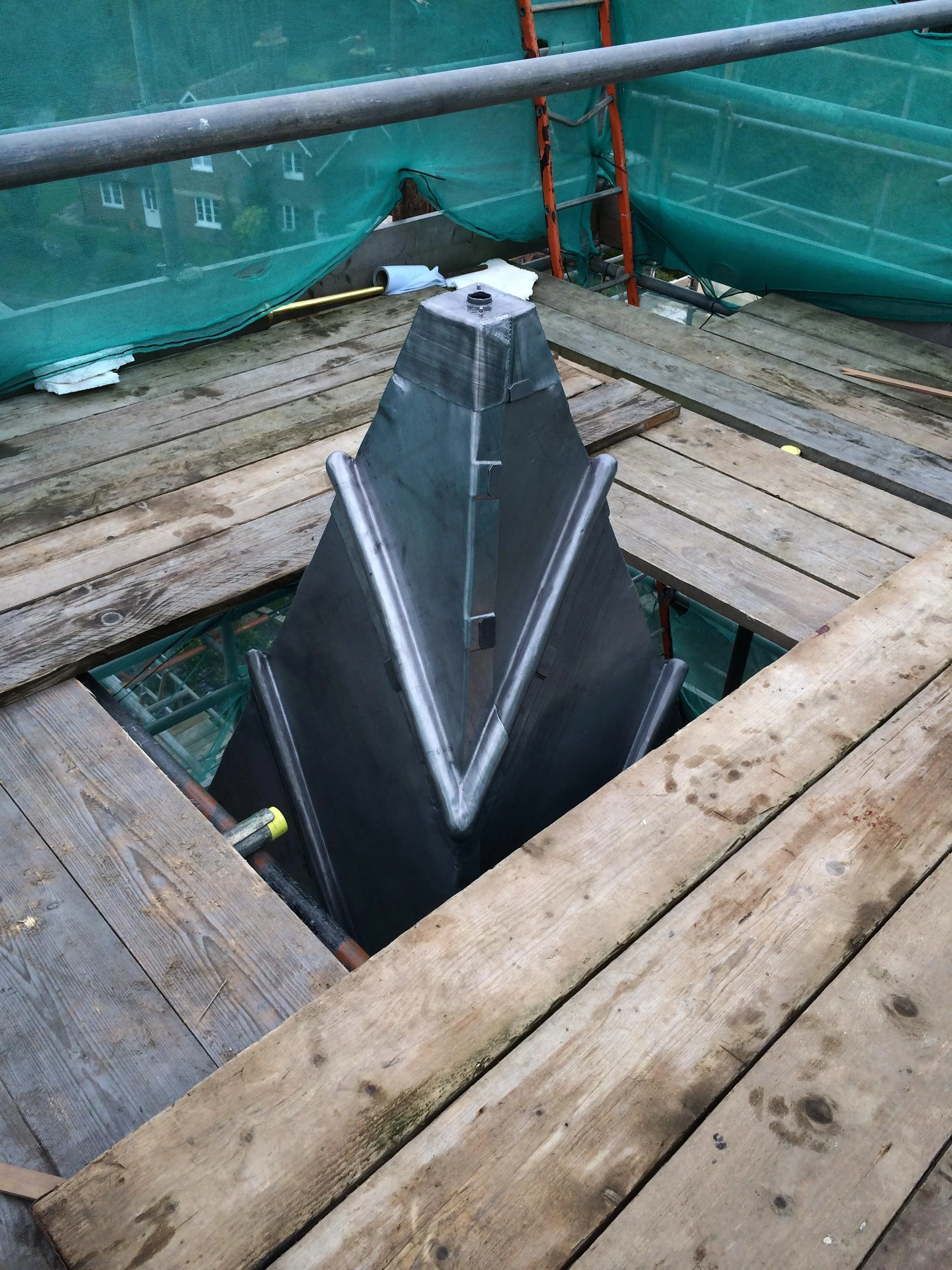 Construction site with wooden planks and scaffolding, showing a large metallic structure with a pointed top.