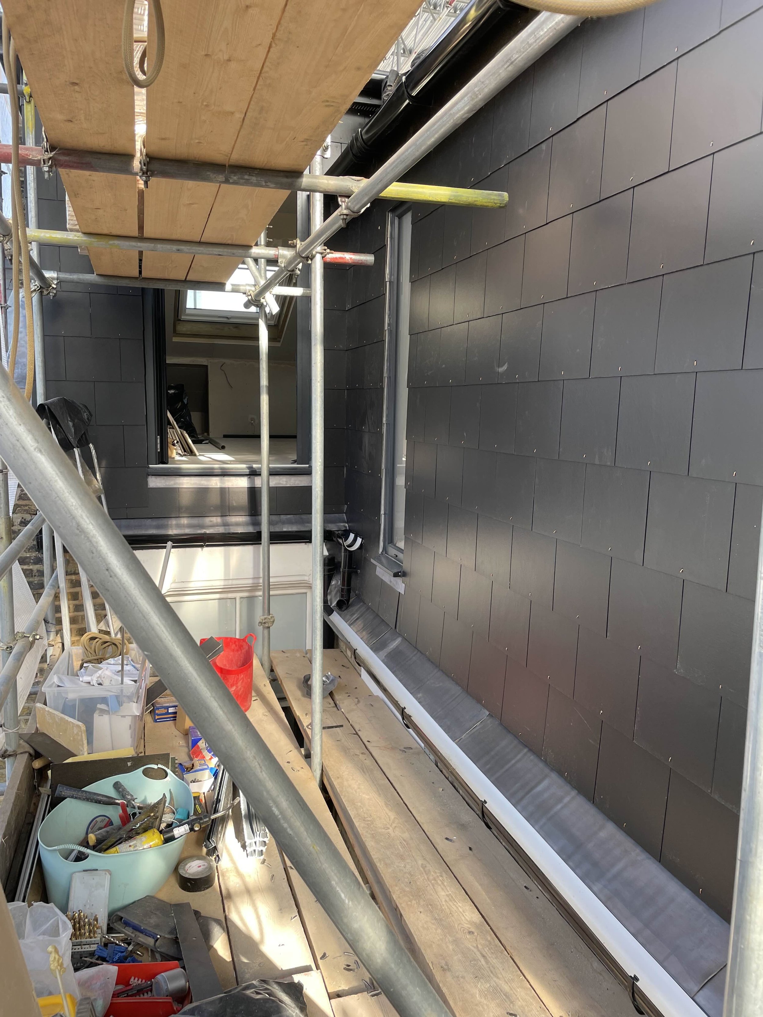 Construction site on a building roof with scaffolding, black exterior wall, window, and construction tools and supplies.
