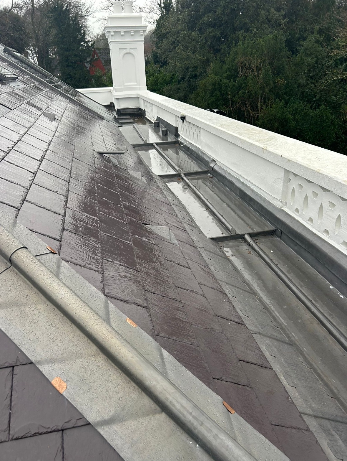 A wet, newly installed slate roof with metal flashing and gutters, and a white decorative railing along the edge of the roof.