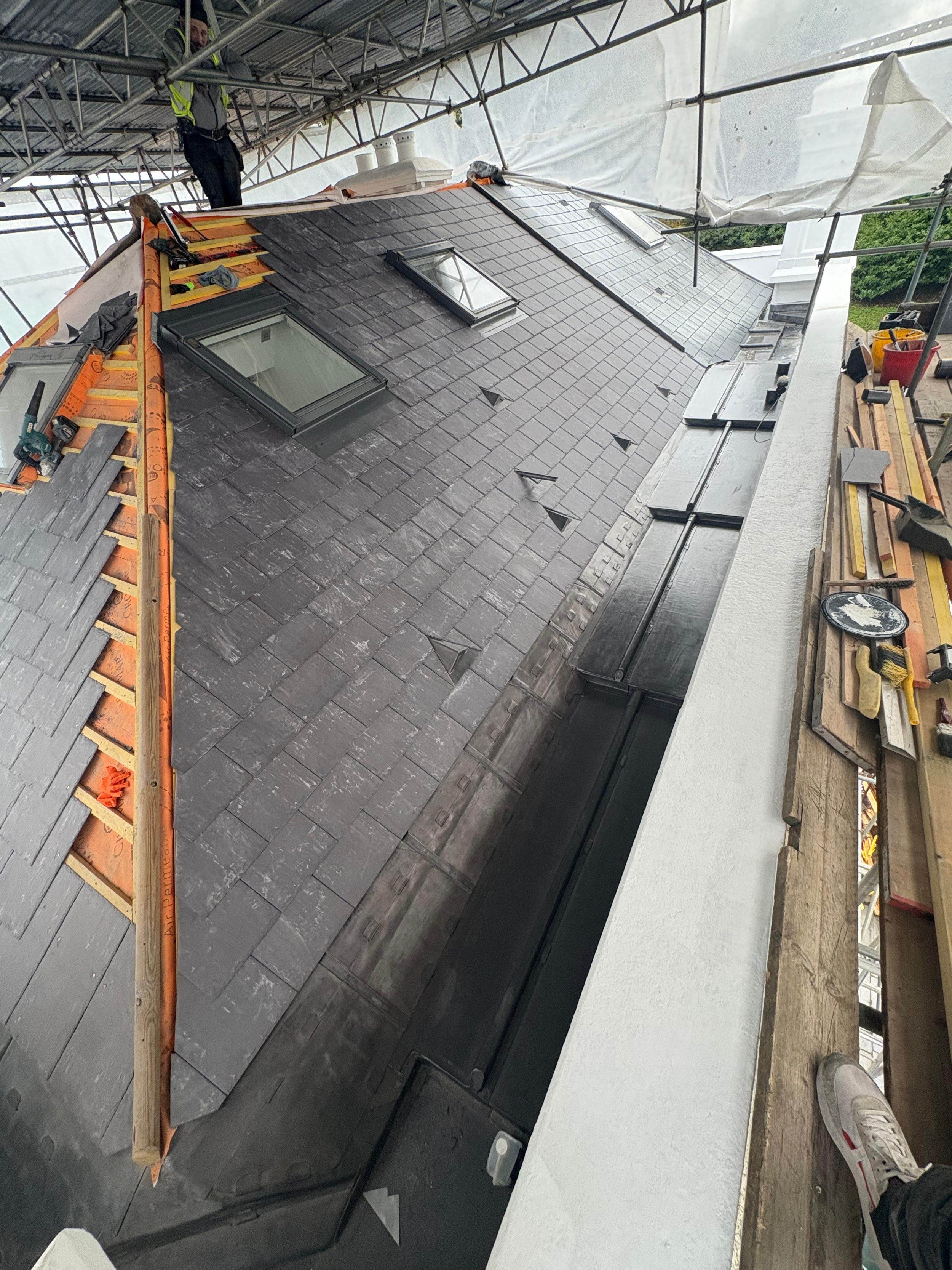 Roof under construction with workers, skylights, and roofing materials.