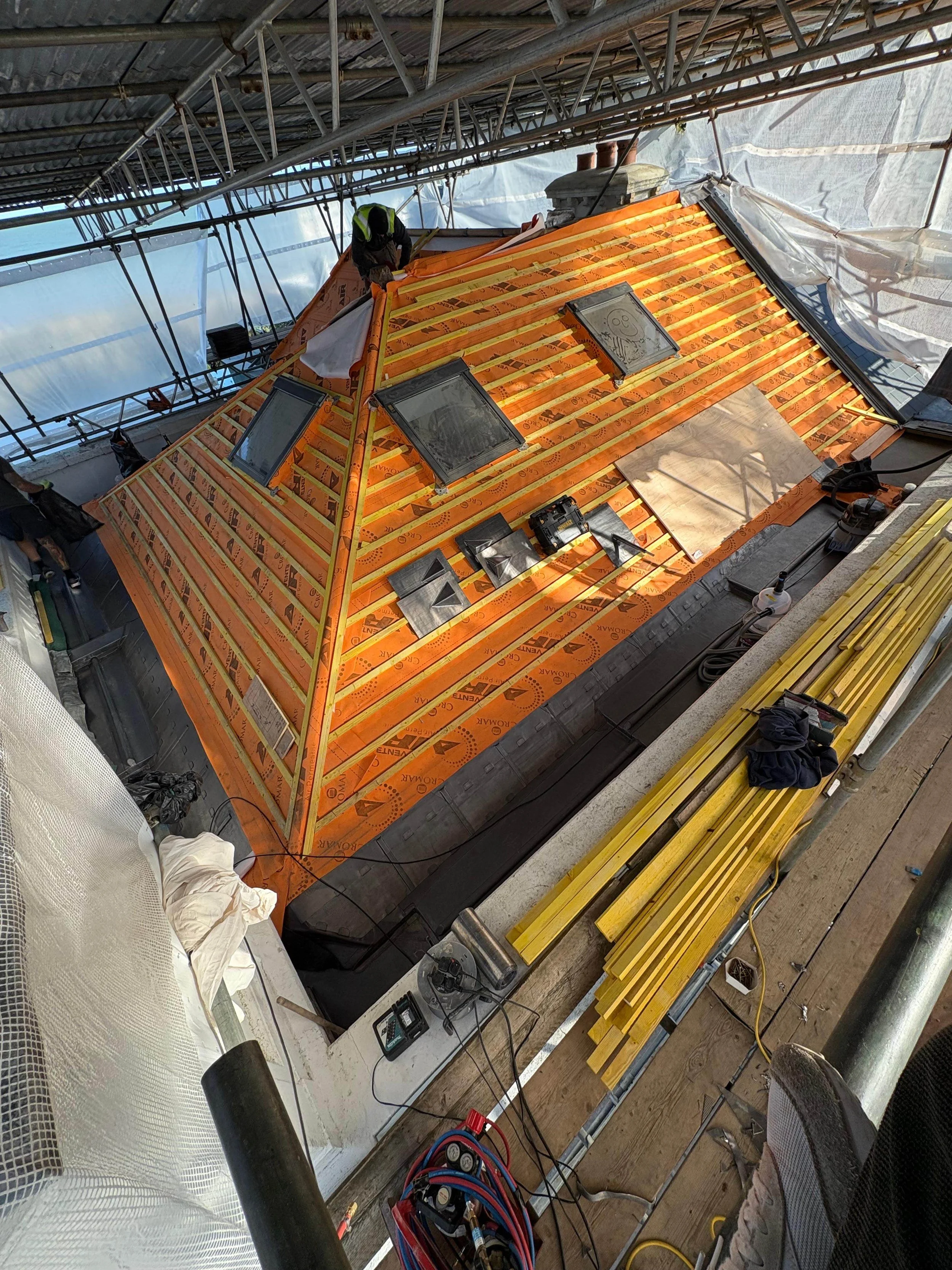 Construction workers installing a new roofing system on a building, with orange insulation and wooden battens.