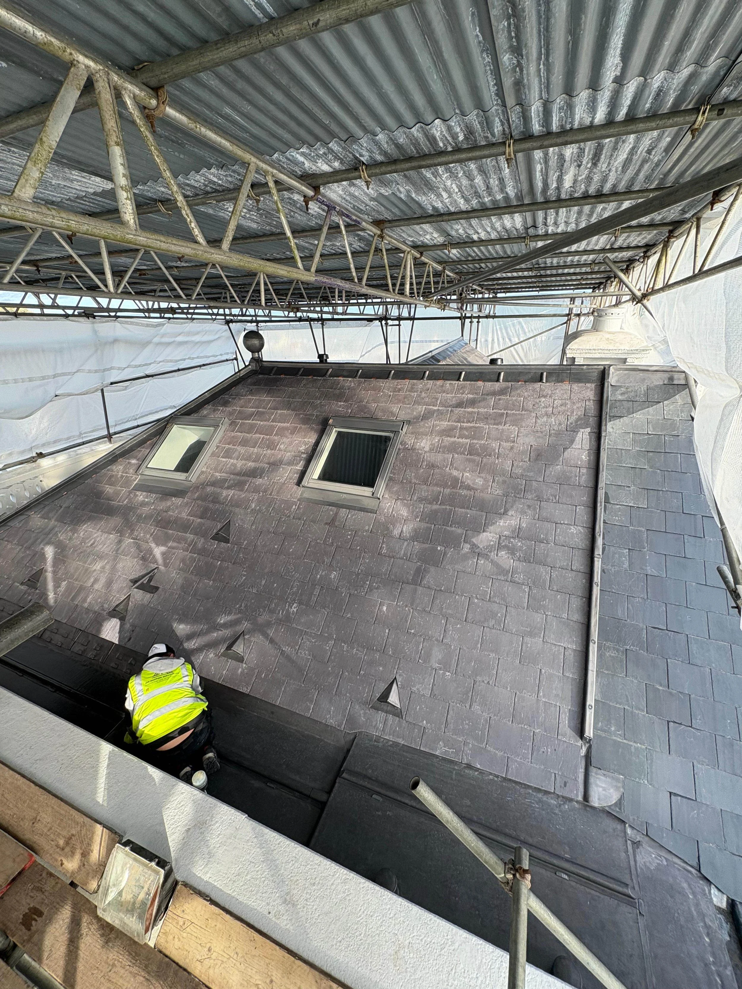 Construction worker inspecting a slate roof from scaffolding on a building under renovation.