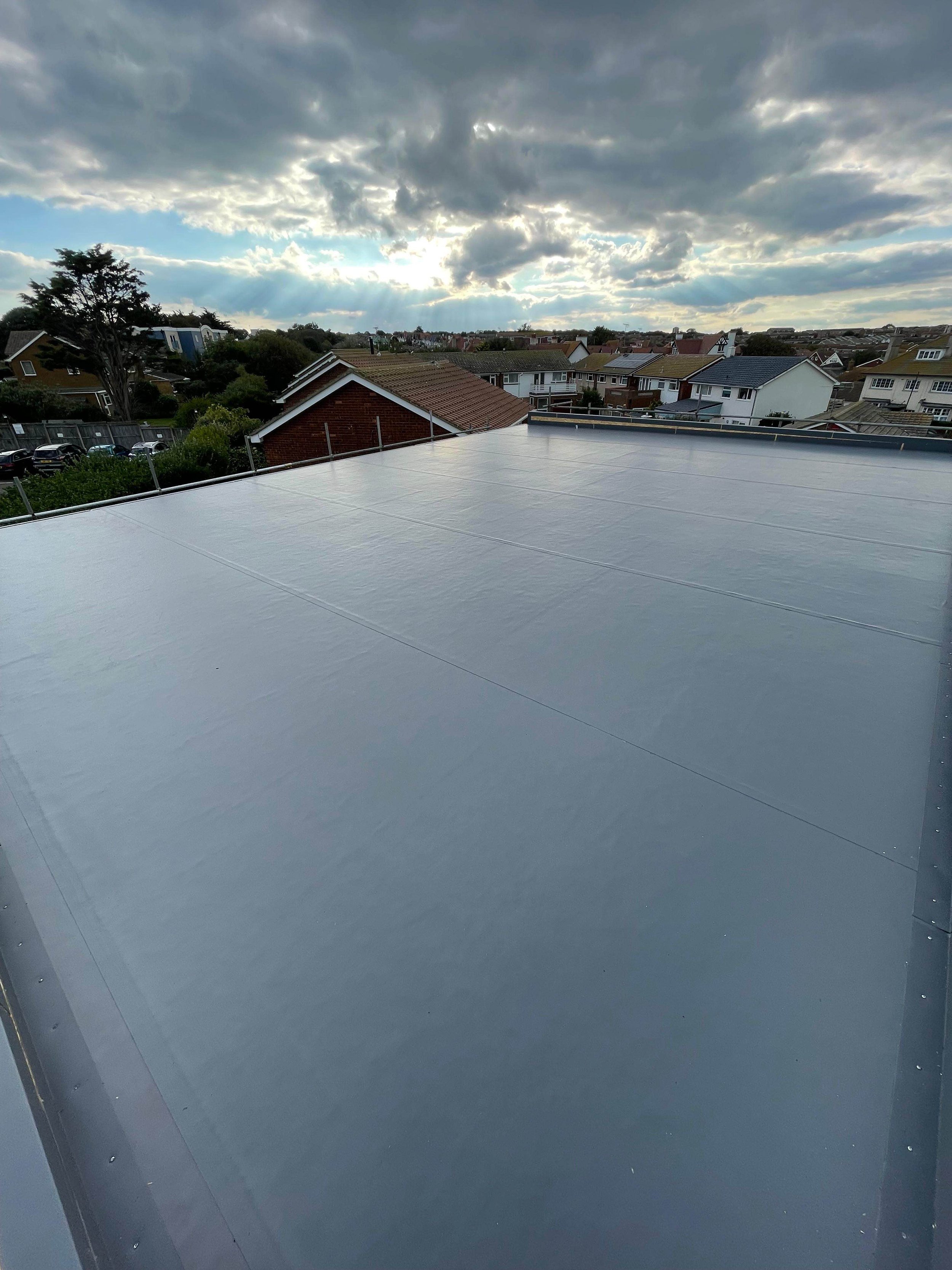 The image shows a large, smooth, metallic rooftop with a suburban neighborhood and cloudy sky with sun rays in the background.
