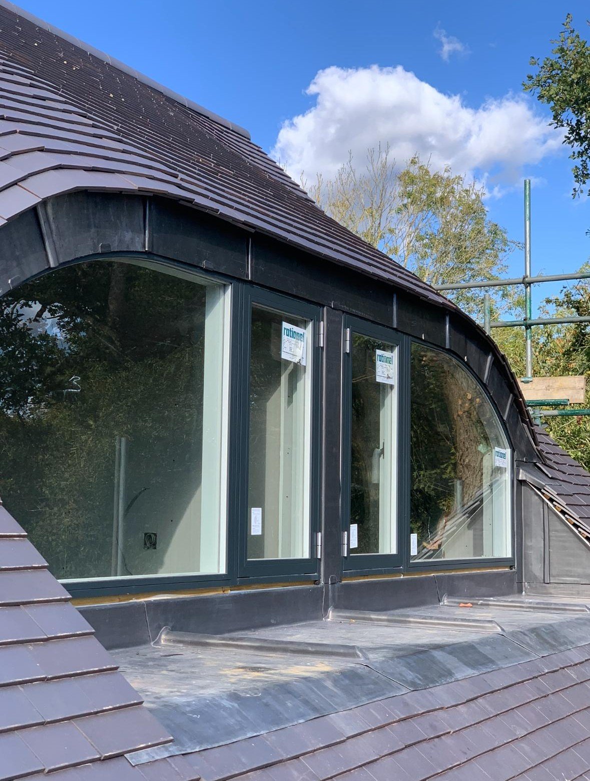 A house with a curved roof and large window openings under a blue sky with clouds.