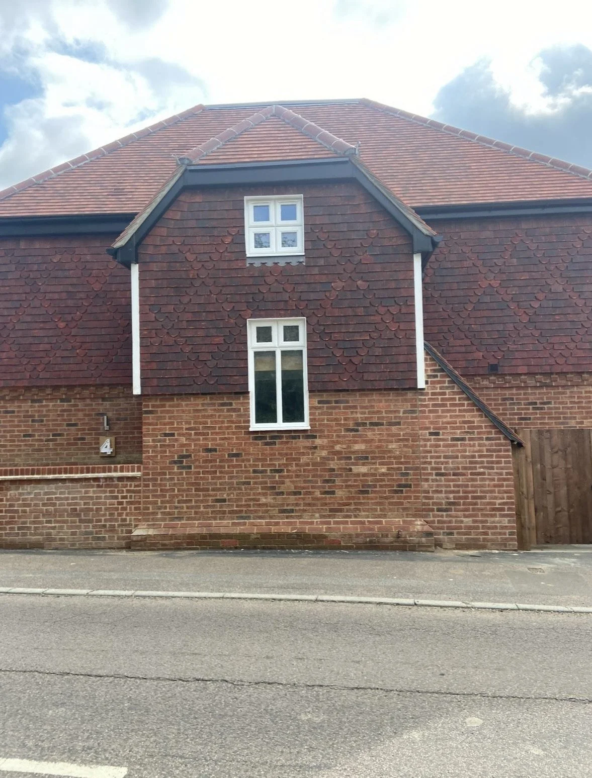 Front of a two-story brick house with a red tiled roof, two small white-framed upper windows, and one tall window on the lower level, with a street in front.
