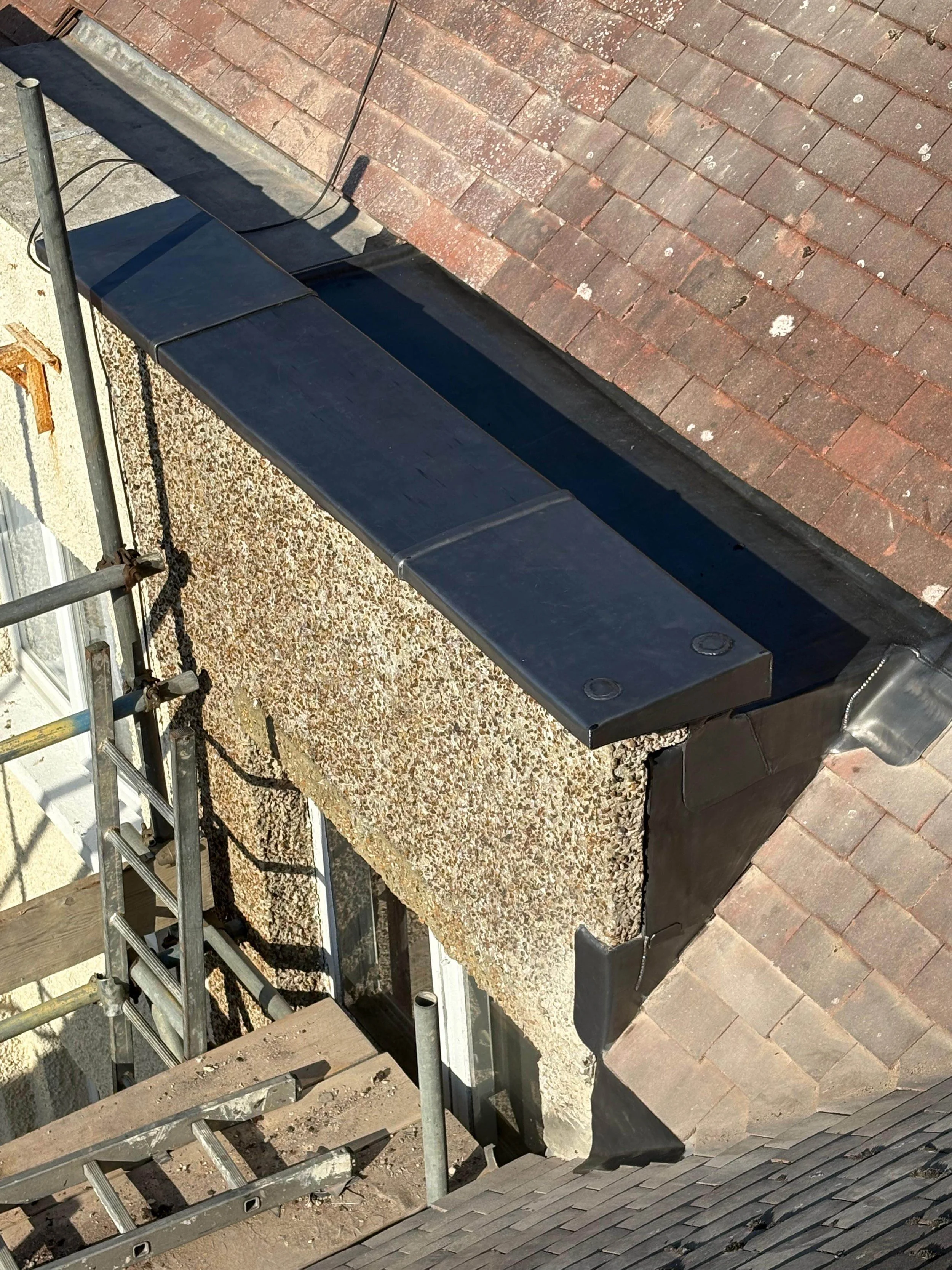 A chimney with a new black cap on a rooftop under construction, scaffolding and tools are visible.