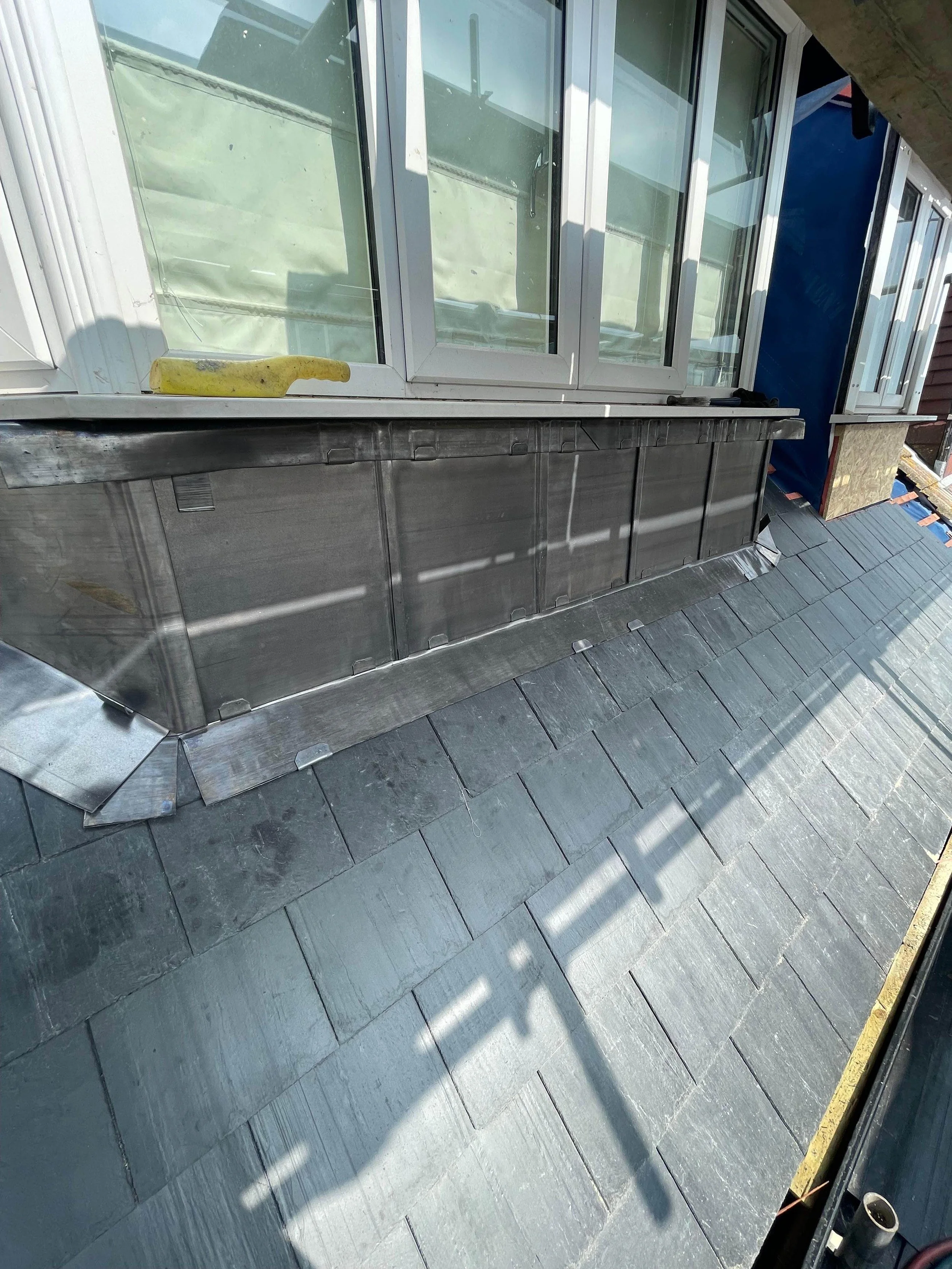Roof construction with black shingles, metal flashing, and a dormer window with white framing. A yellow banana is on the windowsill.