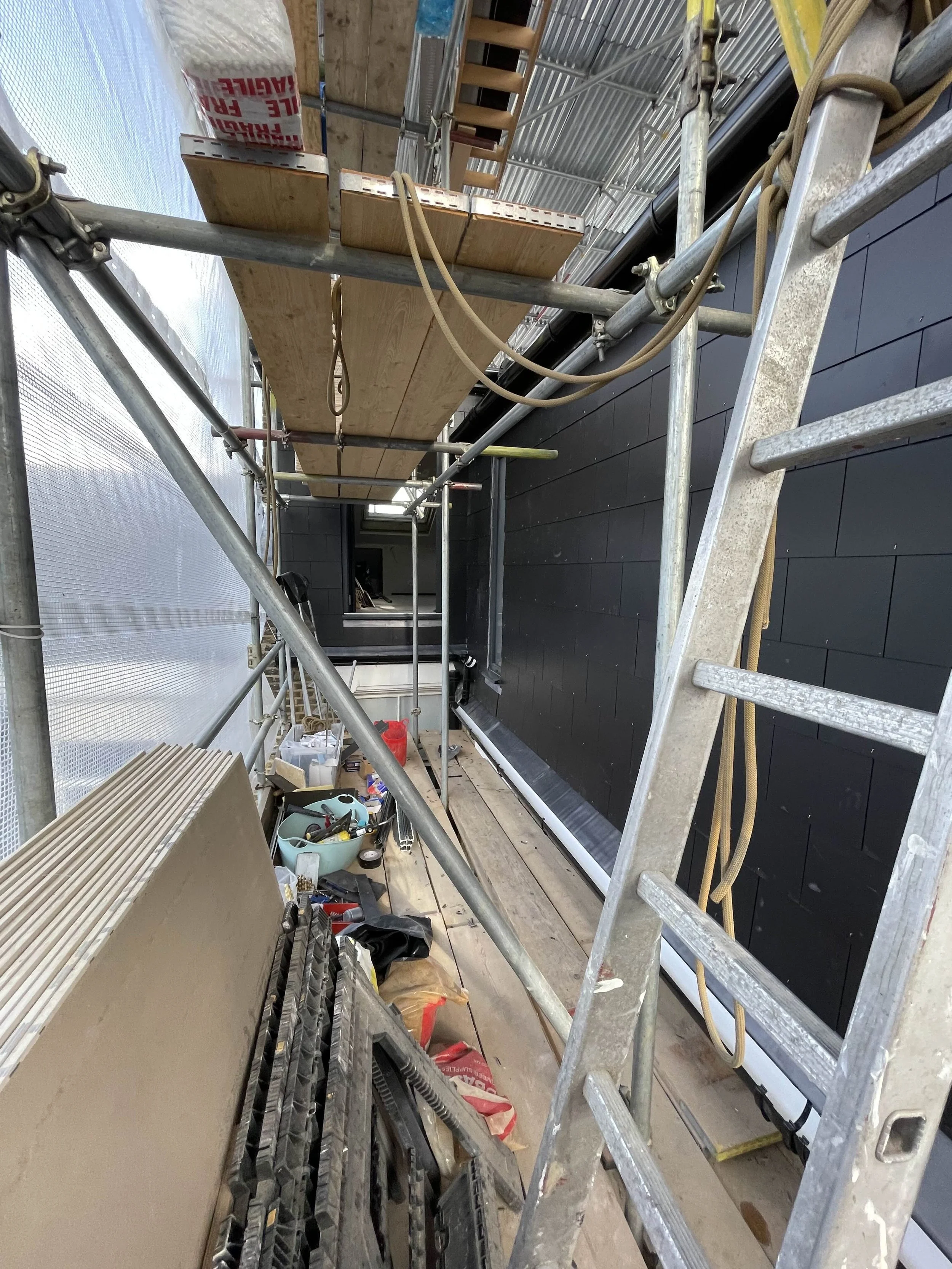 Construction site with scaffolding, ladder, and tools, inside building with black wall and wooden flooring.