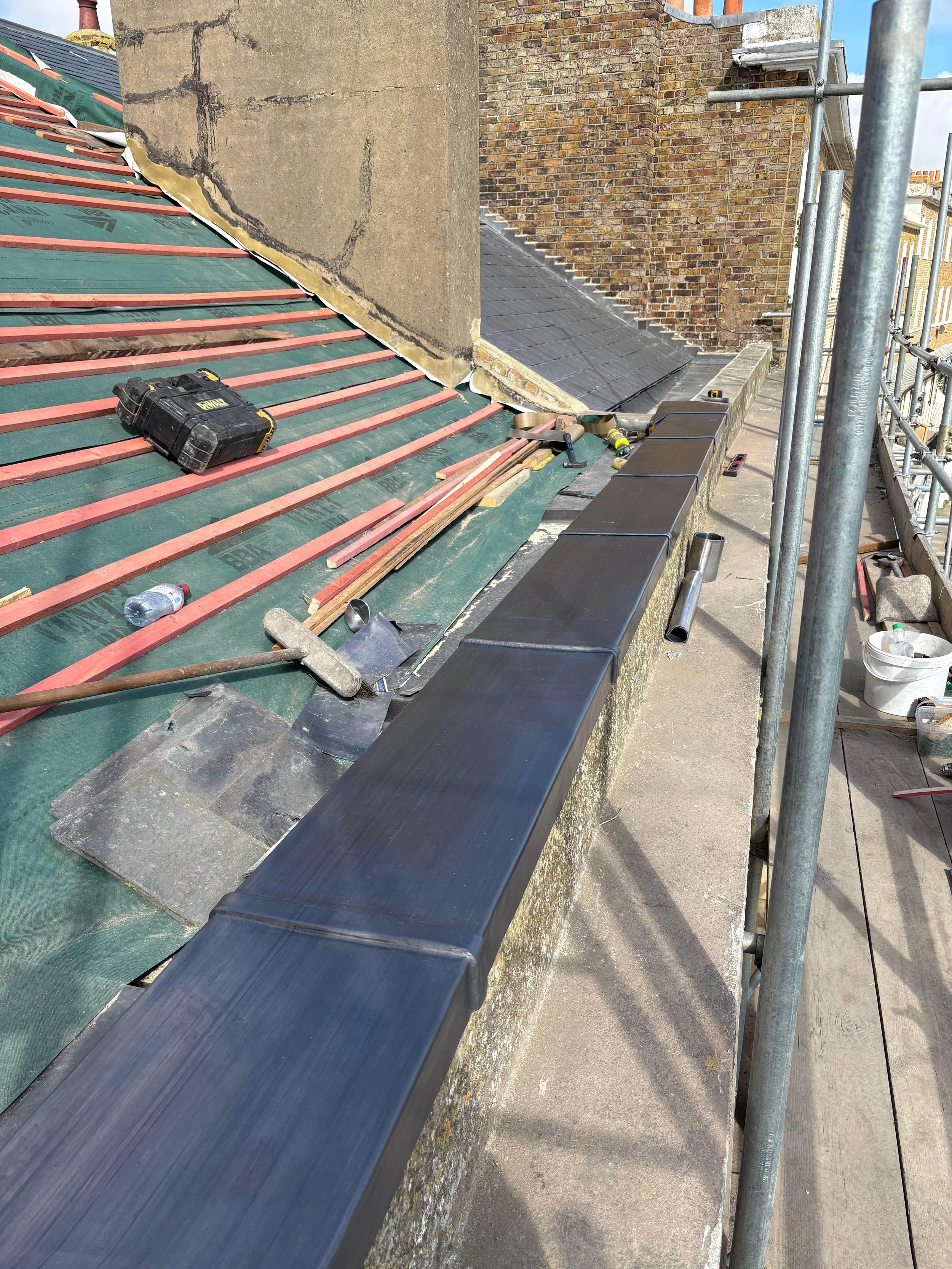 Roof construction with black tiles, tools, and scaffolding, showing work in progress.