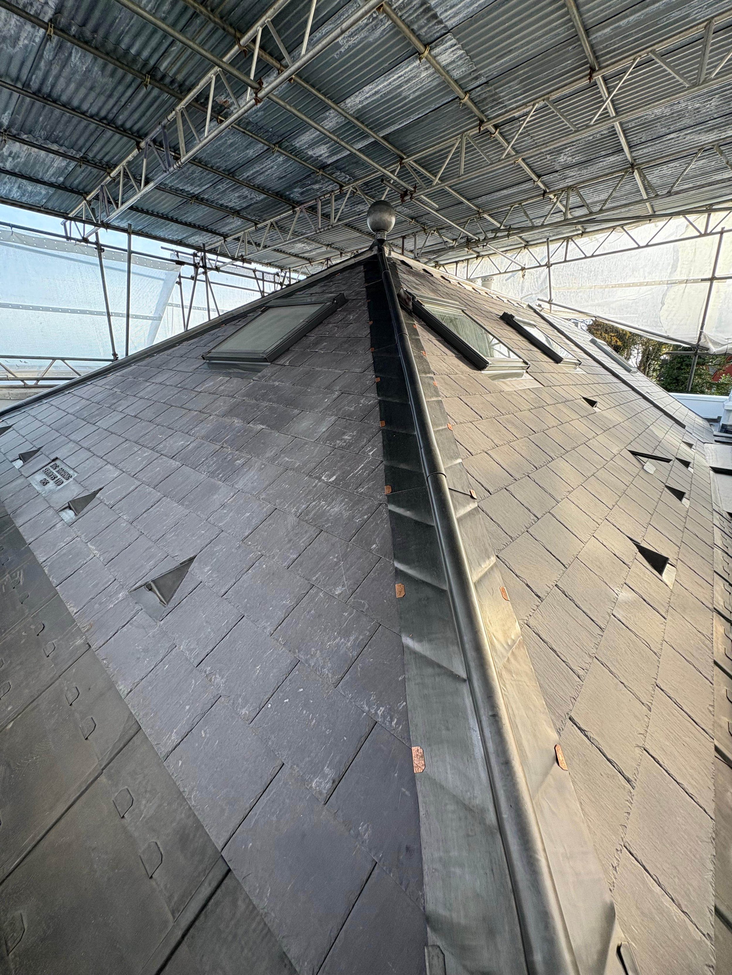 Photo of a steep roof with slate shingles and skylights, under construction scaffolding.