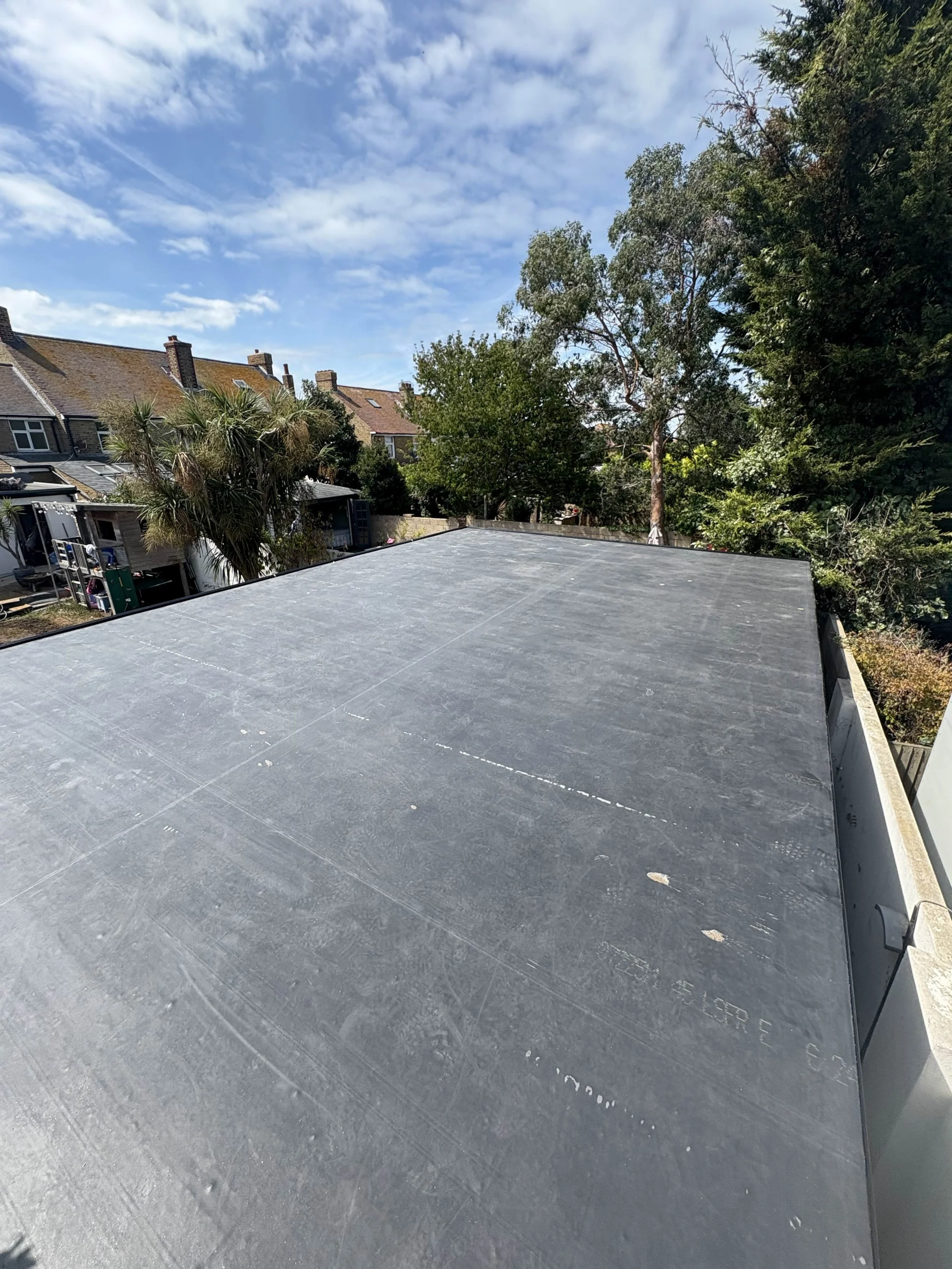 View of a flat rooftop with some trees and houses in the background under a partly cloudy sky.