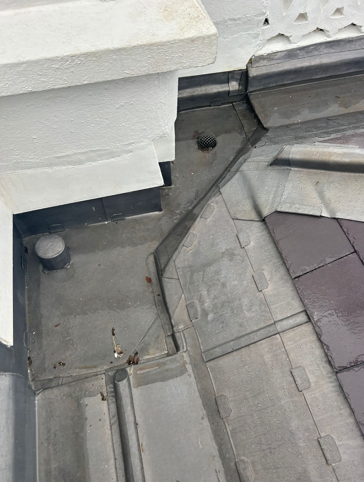 Roof with flashing, vents, and drainage components, including two circular vents and a drain, on a gray surface.