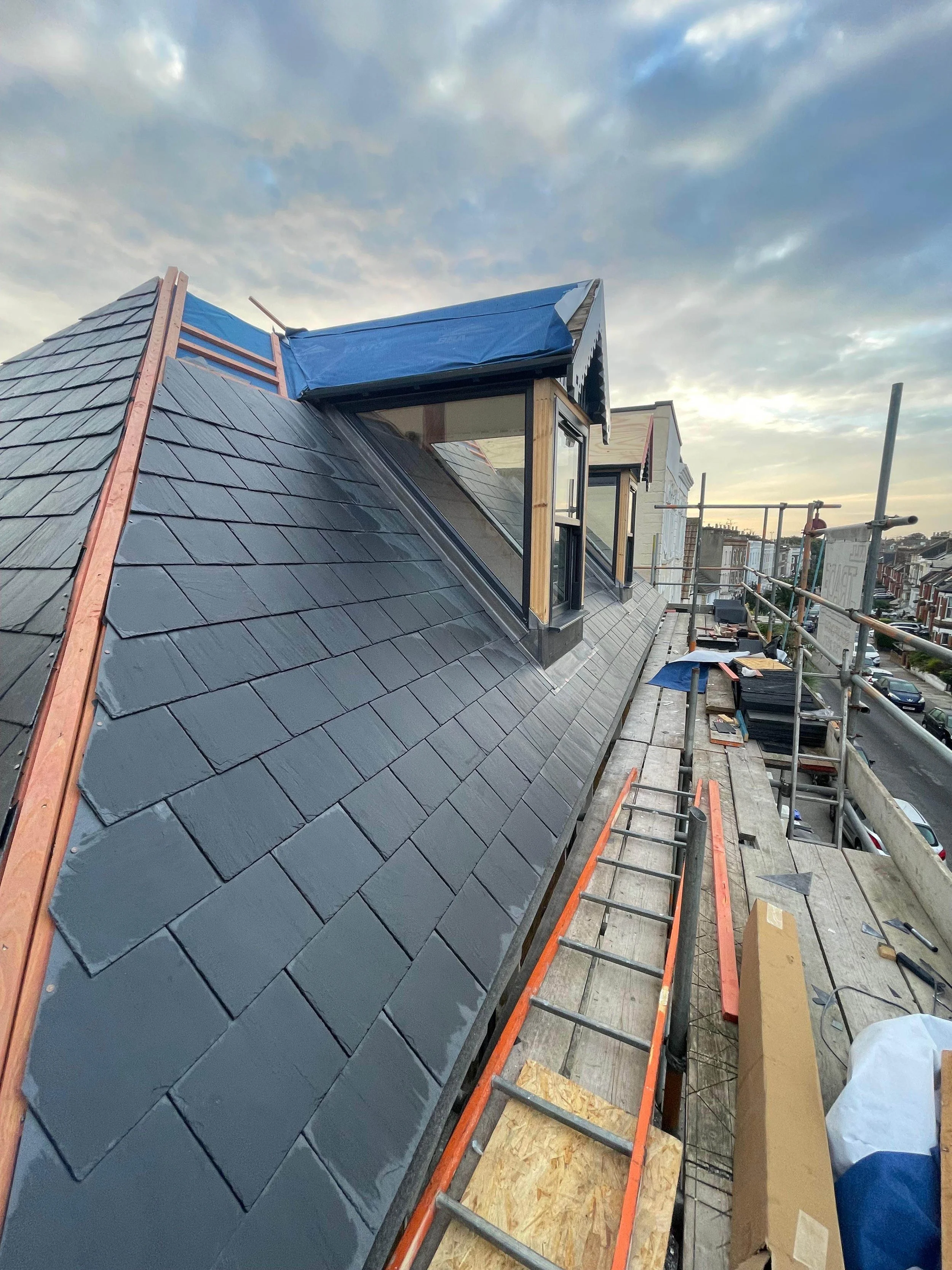 Roof construction with new slate tiles and a dormer window, scaffolding and construction materials on a city street.