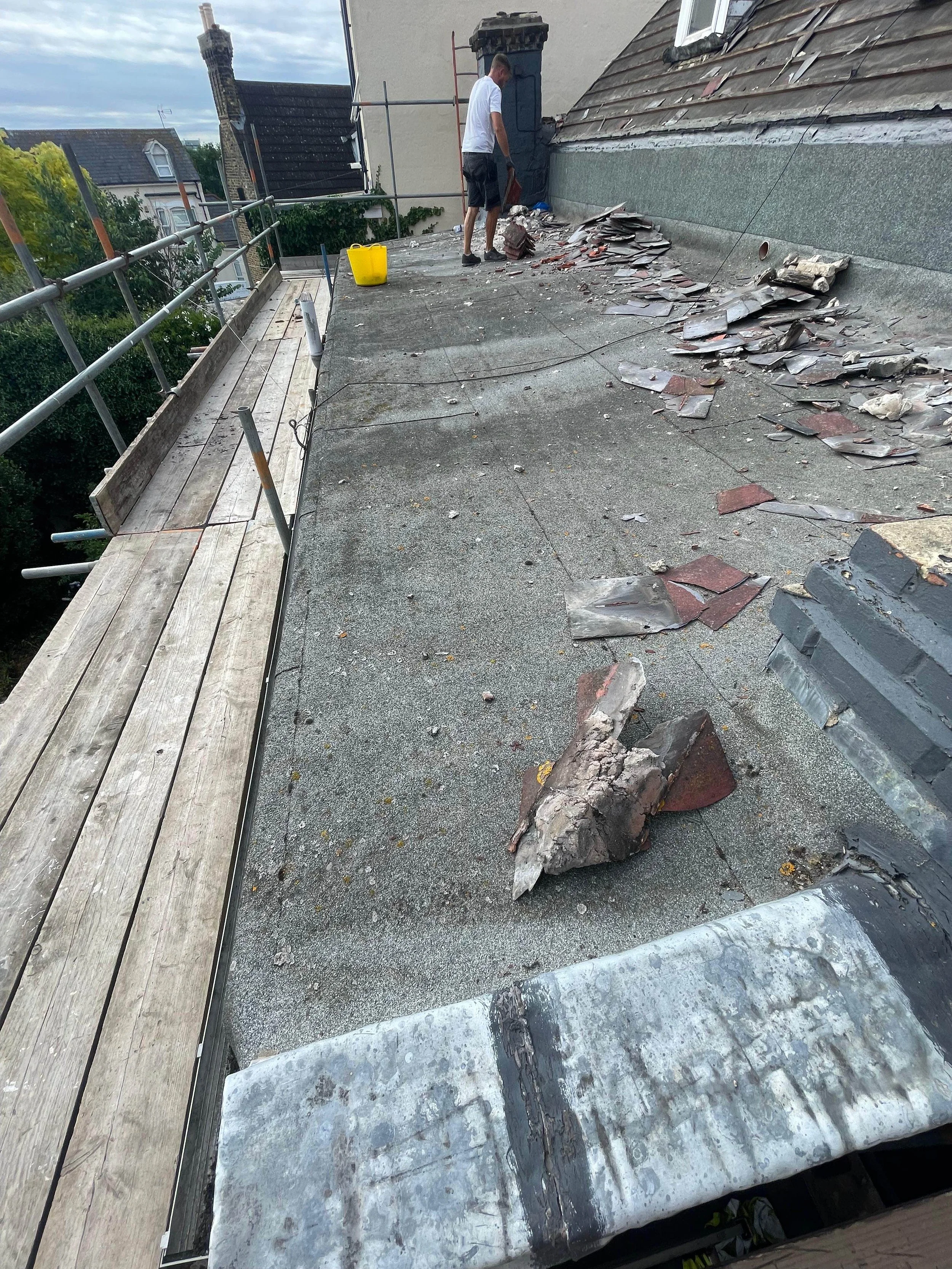 Person on a rooftop with debris and broken tiles, scaffolding, and a wooden platform, as a construction worker repairs or inspects the roof.