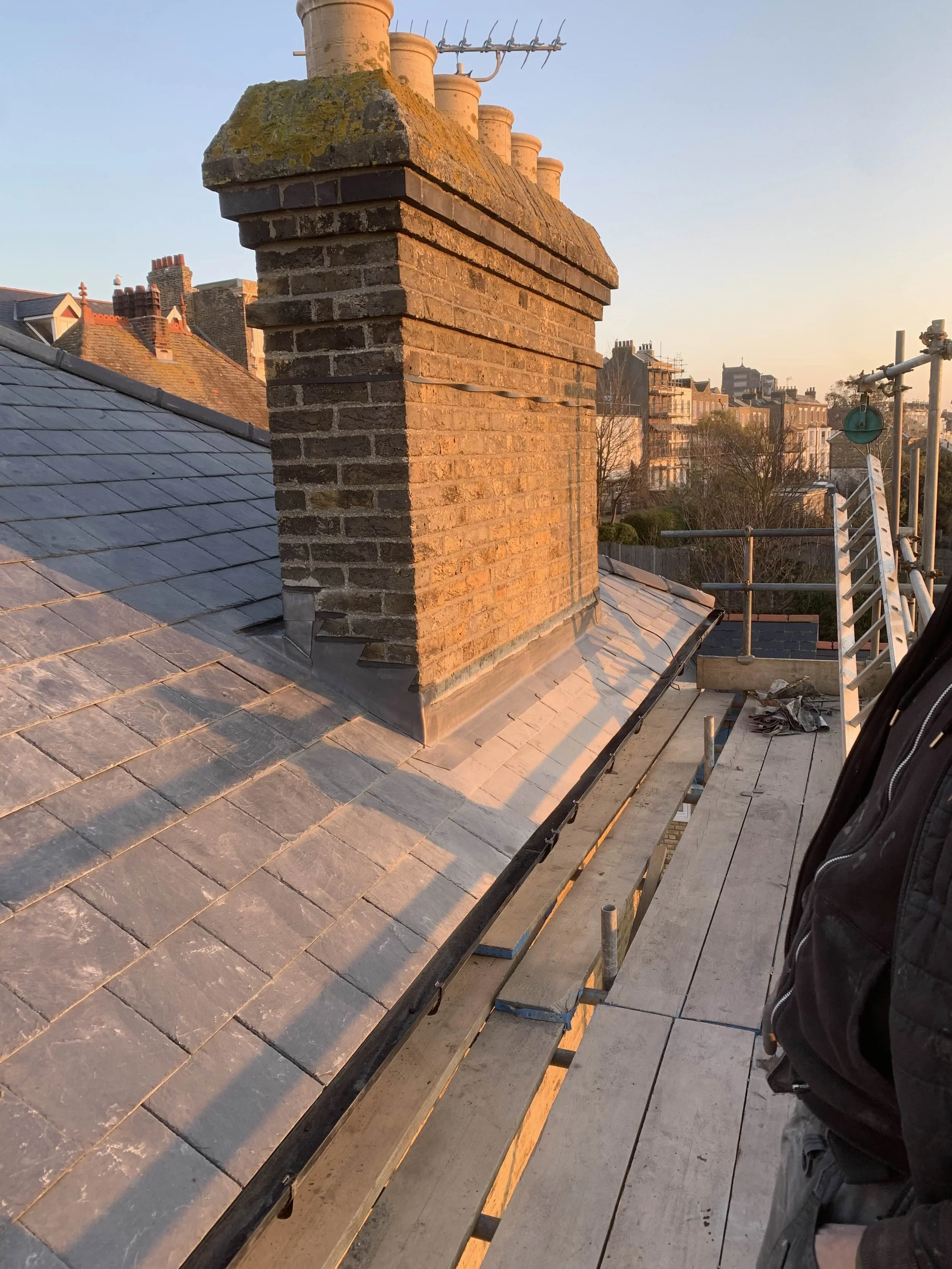 Roof with chimney and scaffolding during construction or repair, with protective wooden planks and tools.