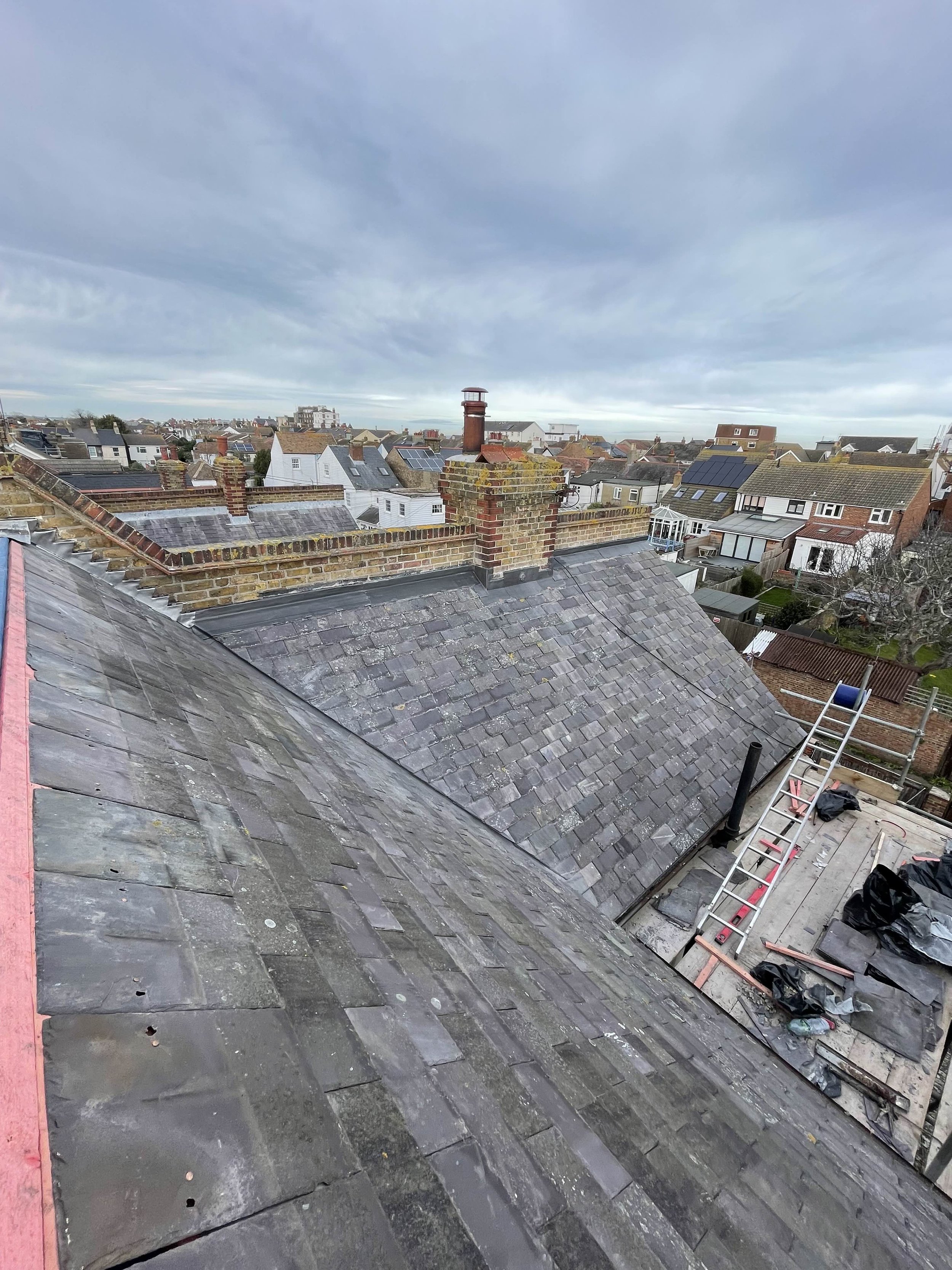 View of rooftops in a neighborhood on a cloudy day, with brick chimneys and a construction scaffold on a building.