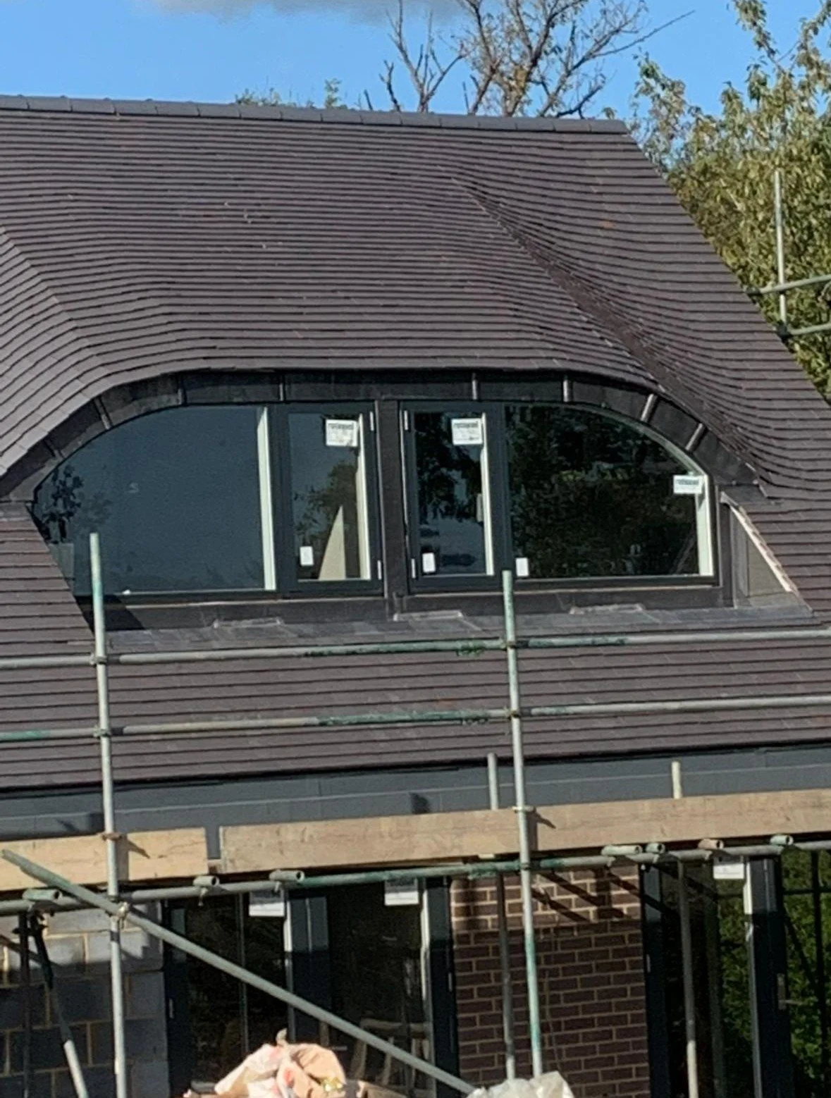 Construction site with a house roof featuring a large arched window and scaffolding around the building.