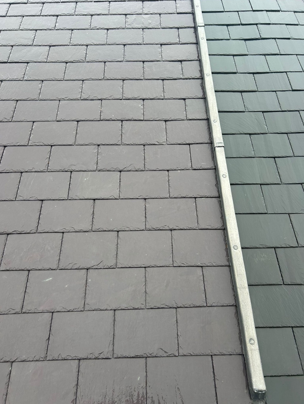 Close-up of a roof with two different shades of gray shingles separated by a metal strip.