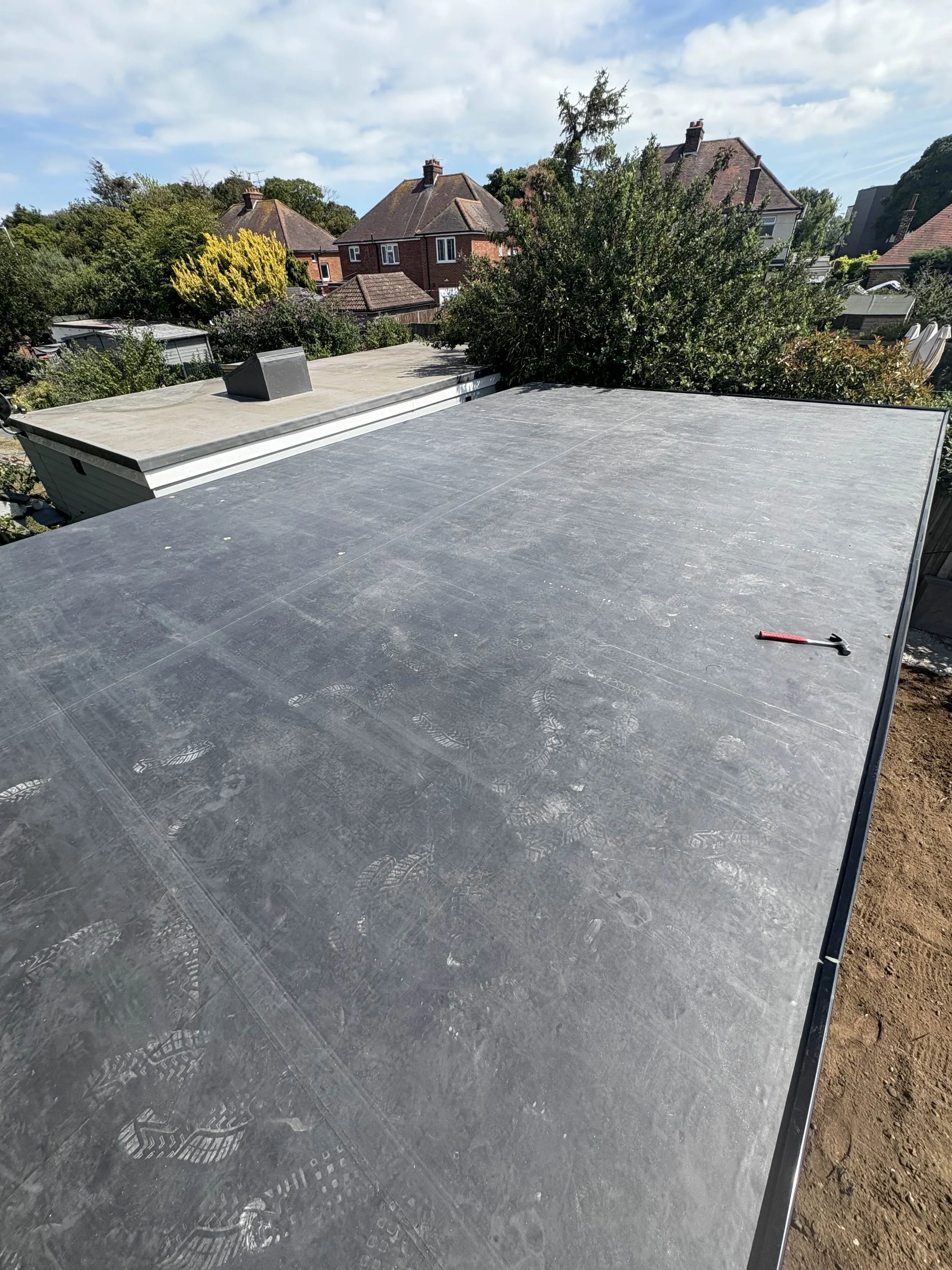 Flat roof with a hammer, in a residential neighborhood with trees and houses in the background.