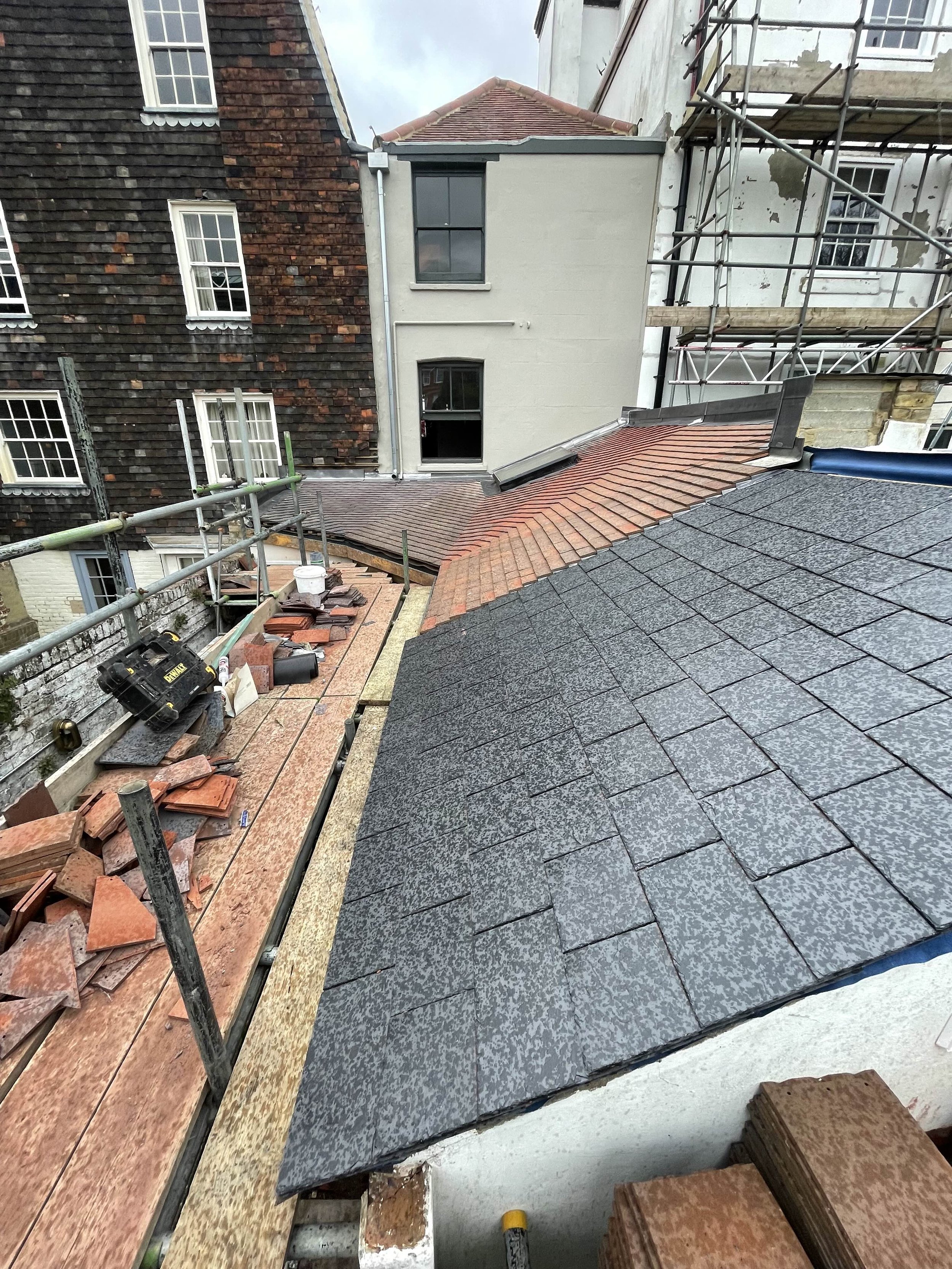View of rooftops with roofing work in progress, scaffolding in the background, and construction tools and materials scattered on the roof edge.