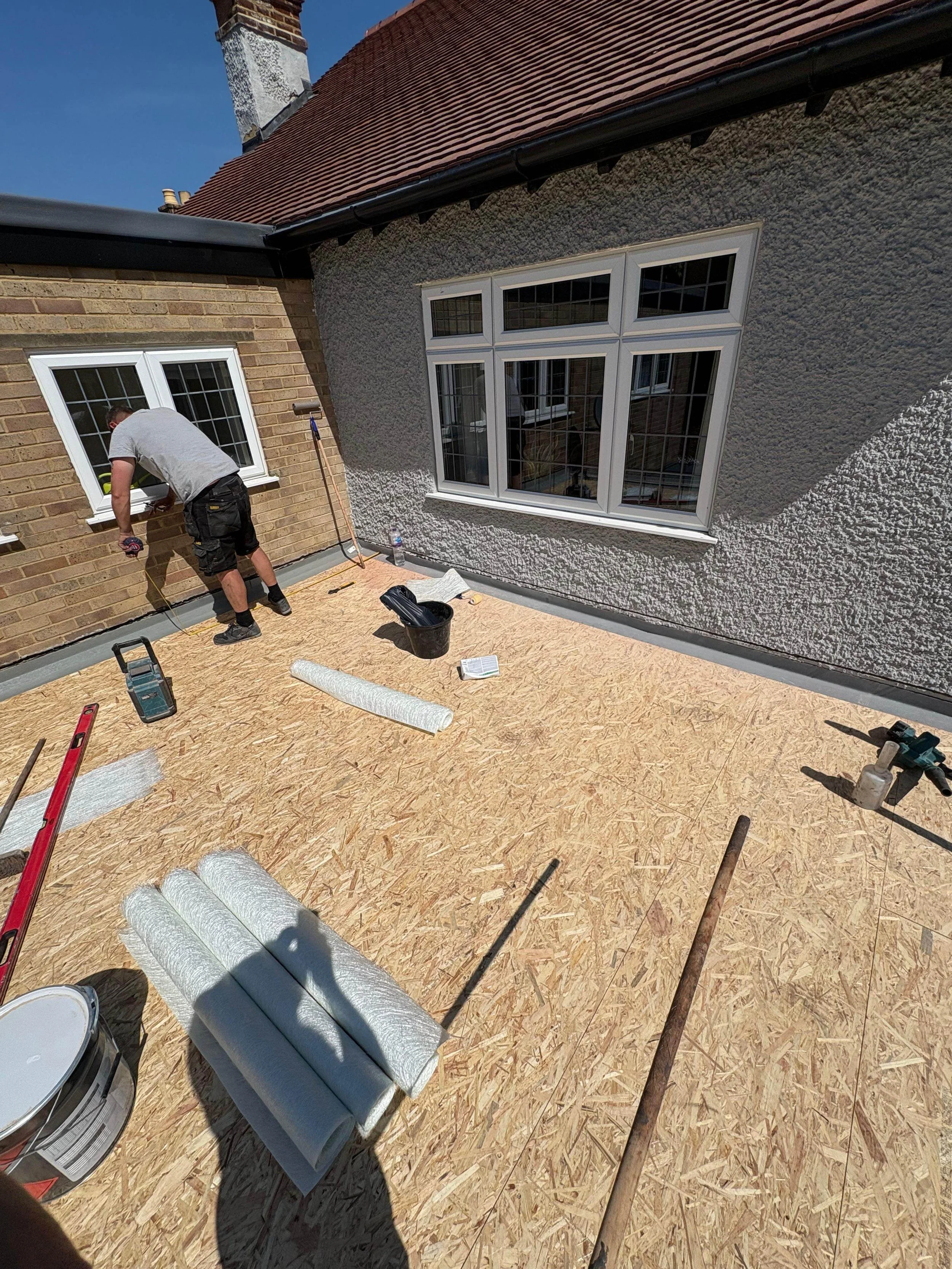 Construction worker installing or repairing windows on a building's roof terrace with tools and materials scattered around.