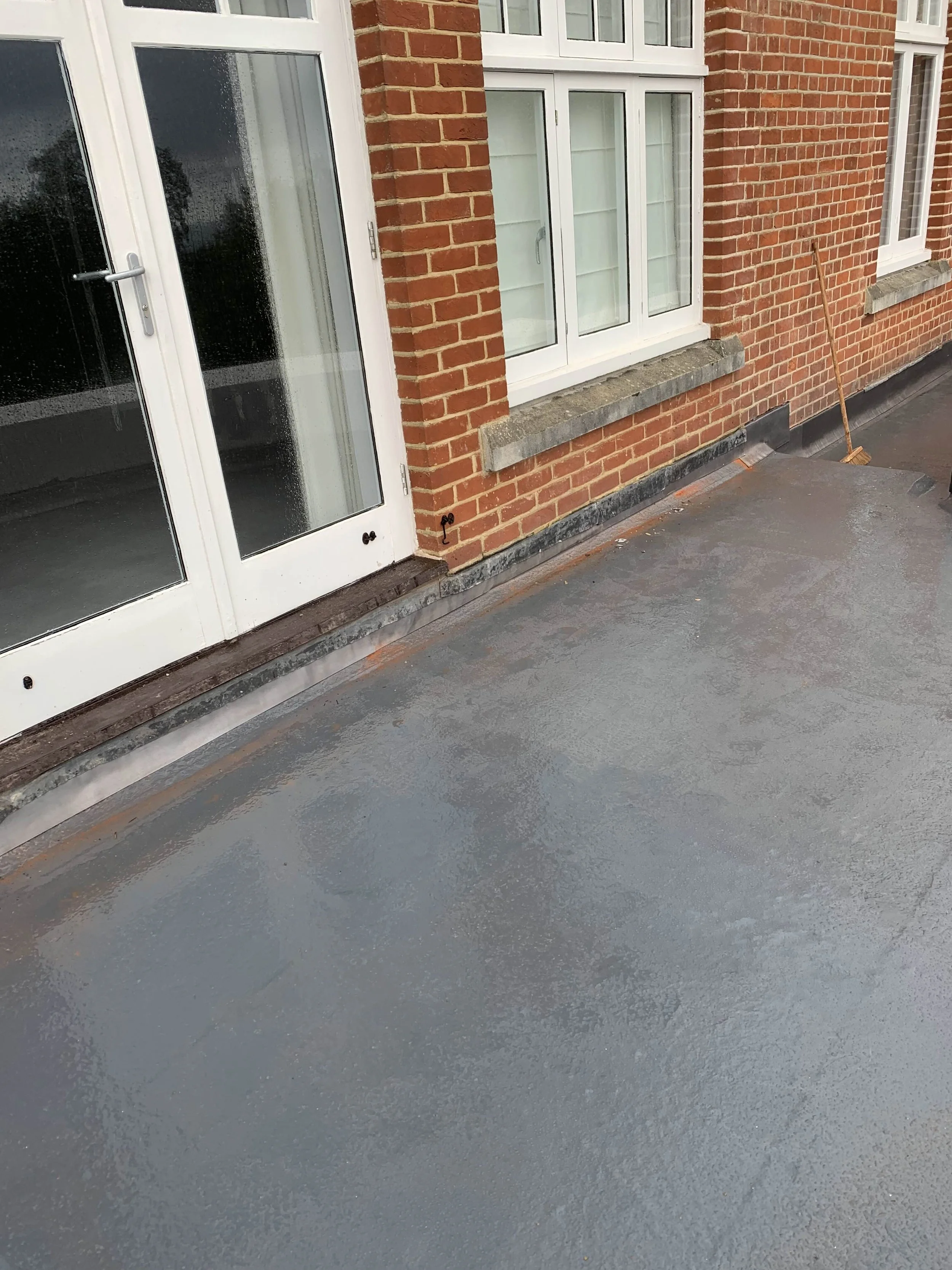 Newly coated gray concrete patio outside a brick house with white-framed glass doors and windows.