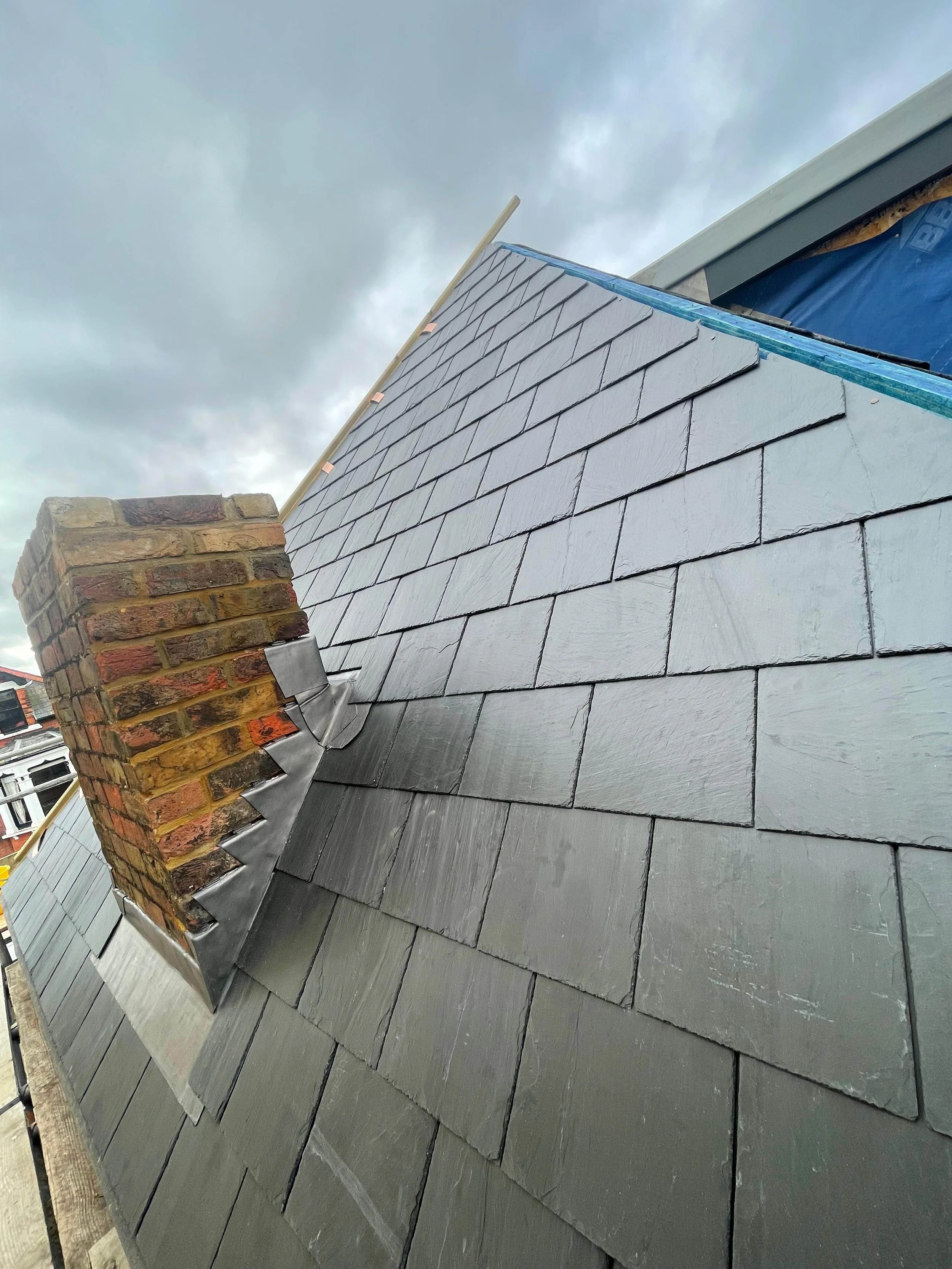 Newly installed slate roof with a brick chimney on a cloudy day.