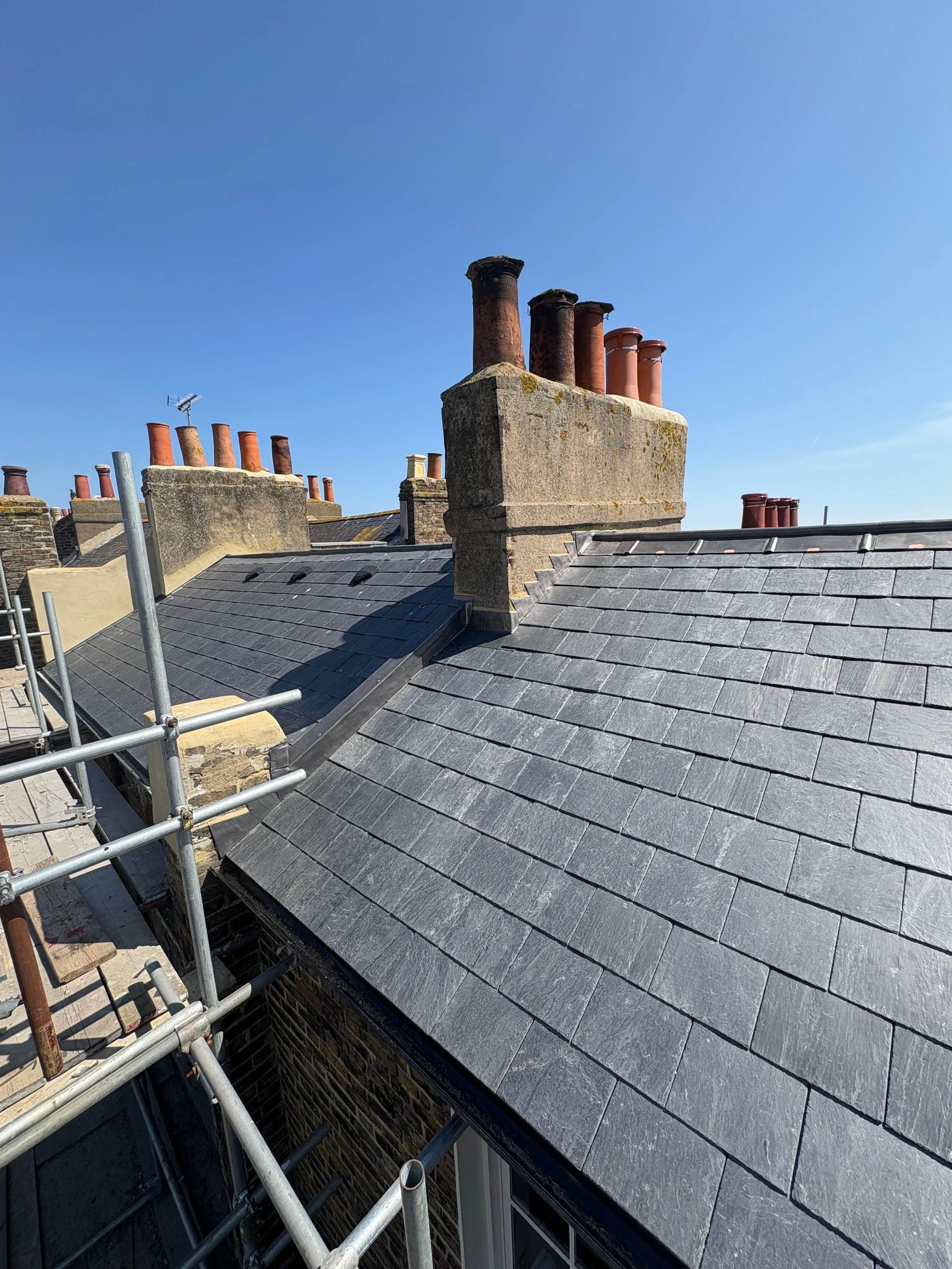 Rooftop with multiple chimneys and slate roofing under a clear blue sky.