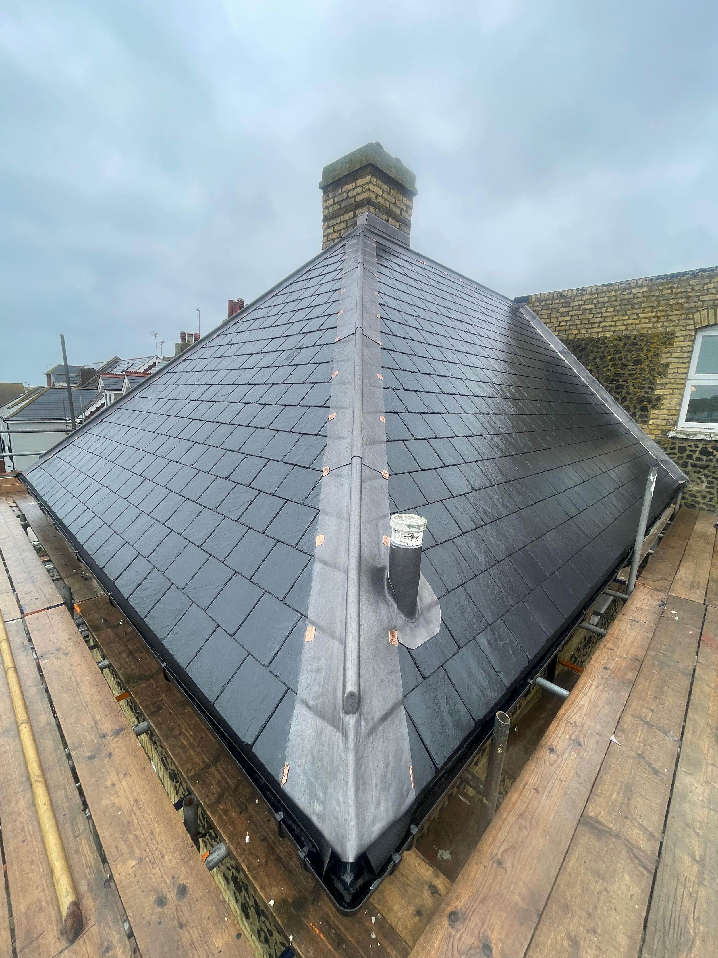 Newly installed dark gray slate roof on a building, with scaffolding and chimney, overcast sky.