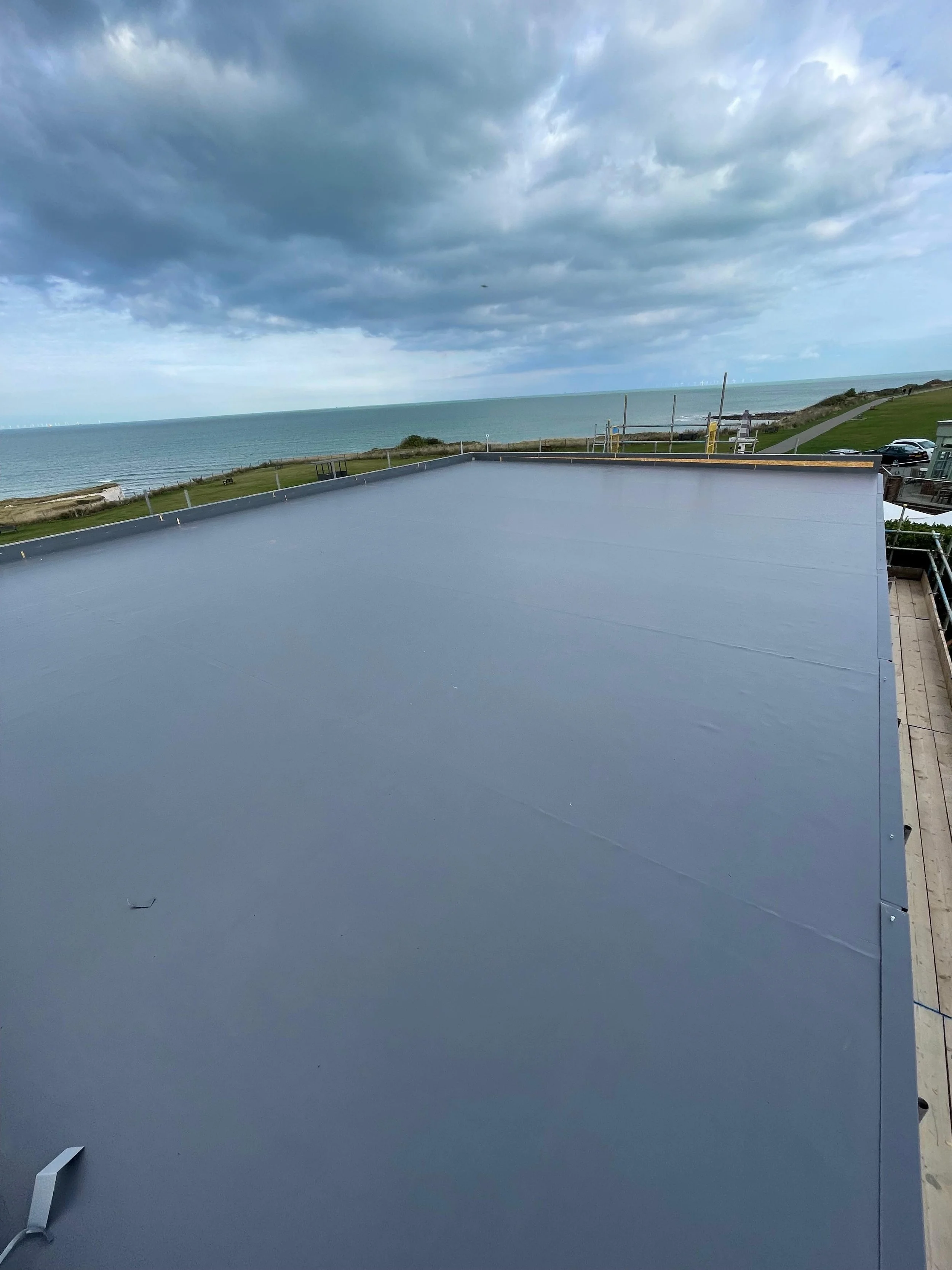 Large flat rooftop with a smooth, shiny surface overlooking a body of water, with a grassy area and cloudy sky in the distance.