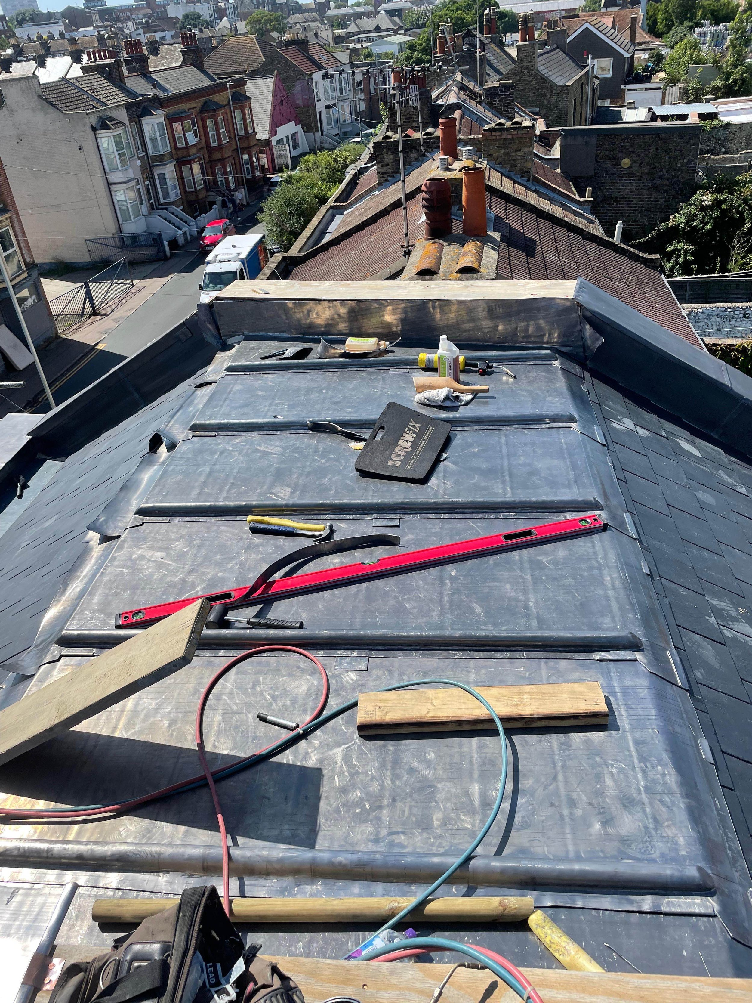 View from a rooftop under construction with tools and materials laid out, overlooking a residential neighborhood with rooftops and streets.