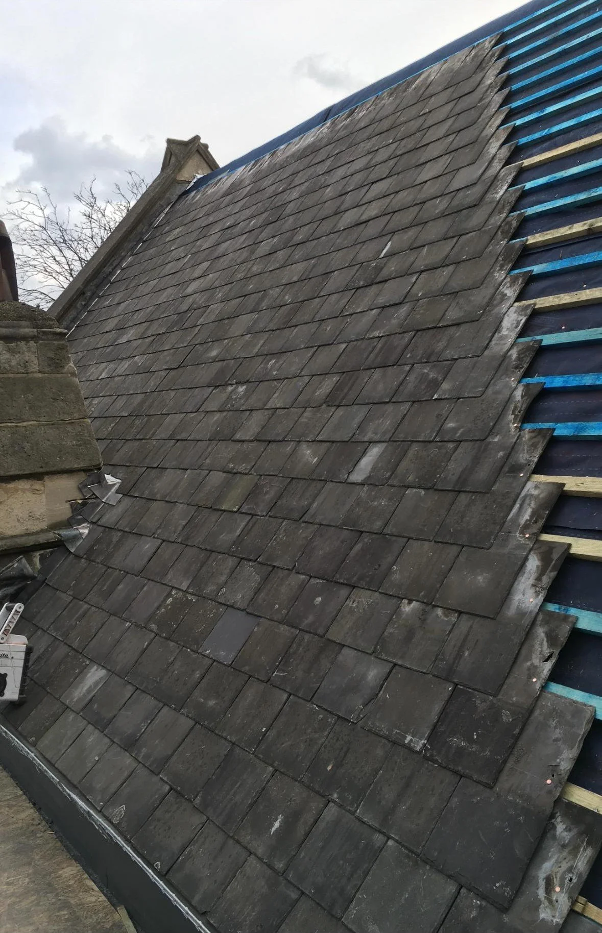 Roof under construction with old gray shingles and new blue underlayment showing underneath.