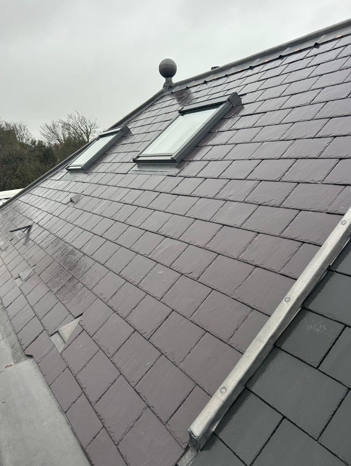 Close-up of a sloped residential roof with new gray tiles and two skylights, under an overcast sky.